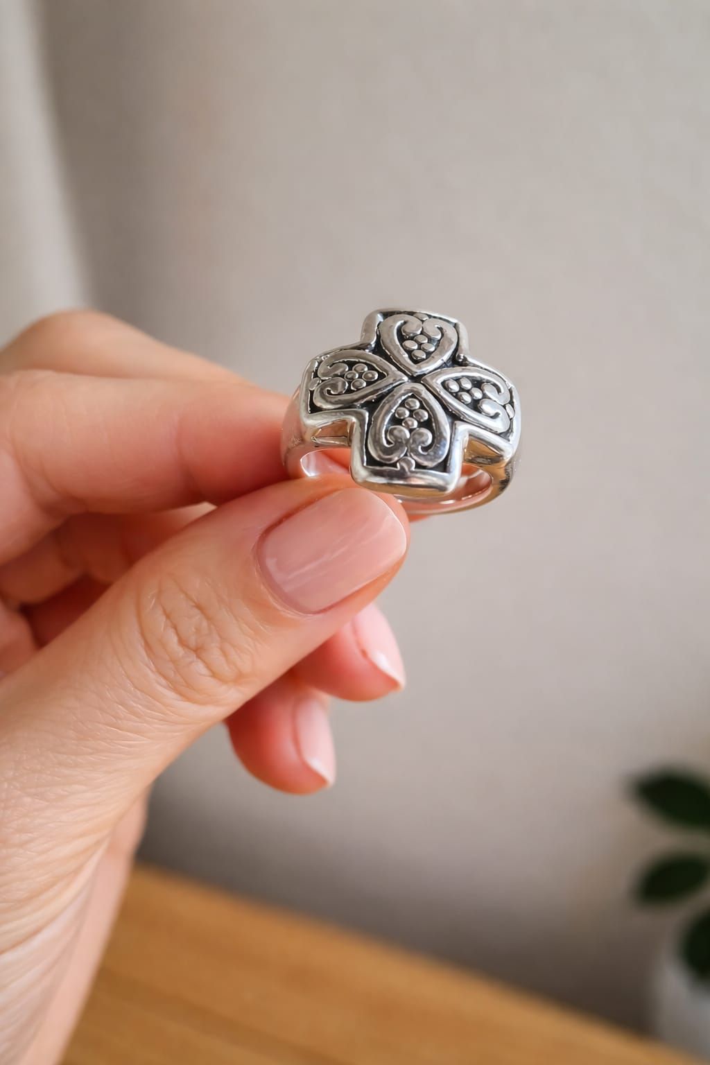 Mano sosteniendo un anillo plateado con forma de trébol con piedras negras y transparentes sobre un fondo suave.