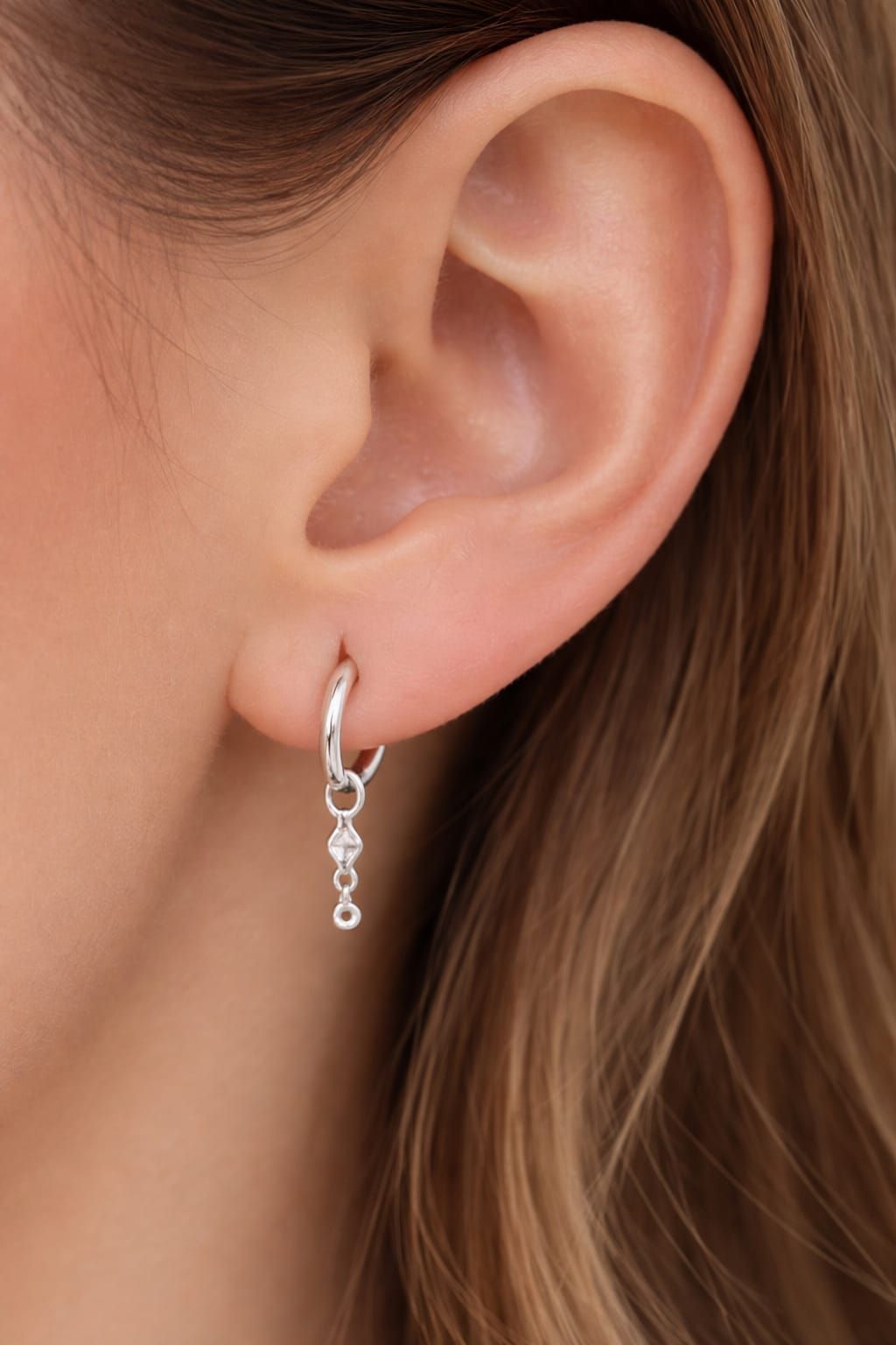 Primer plano de la oreja de una persona que lleva un delicado pendiente de cadena de plata.