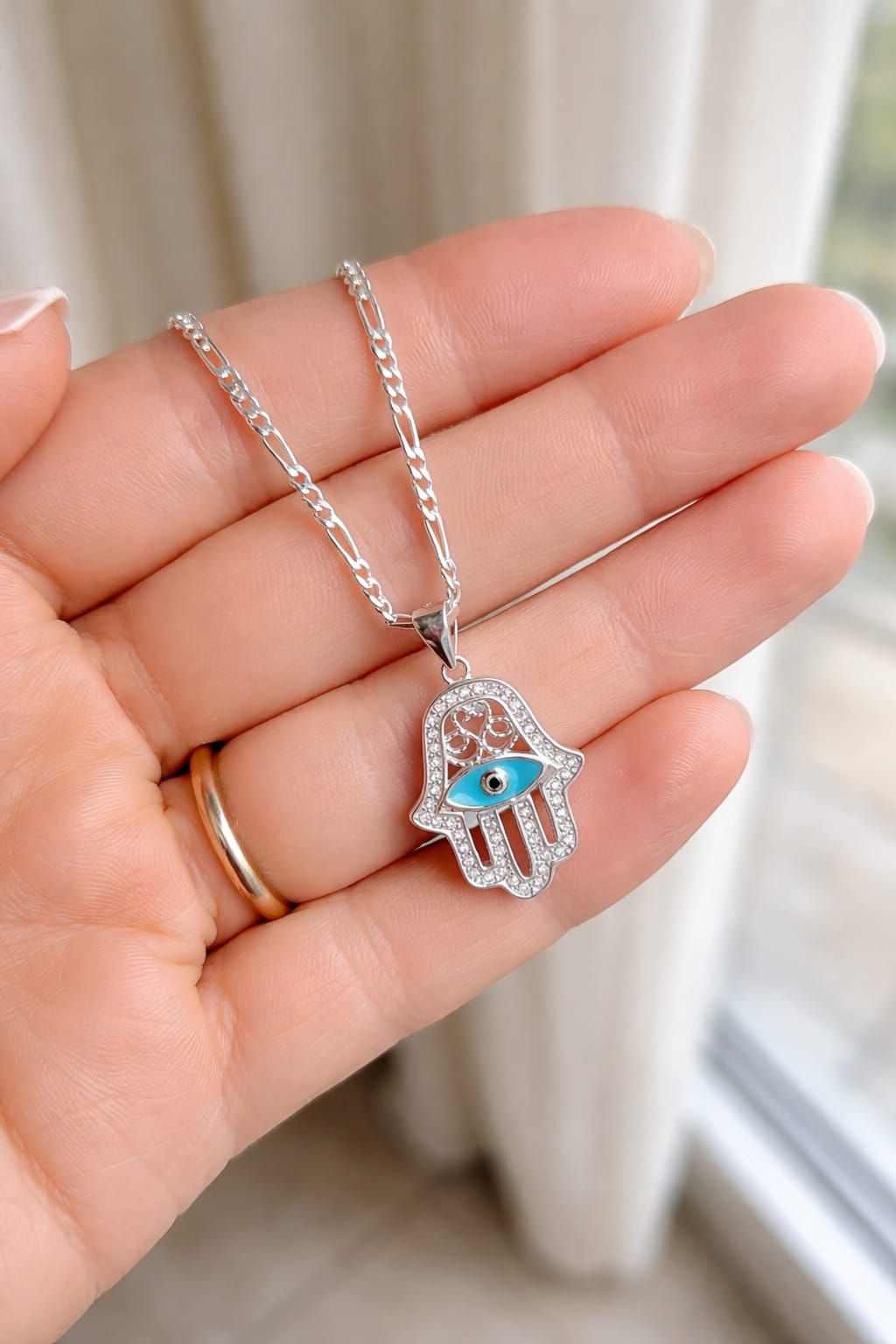 Collar con colgante Hamsa de plata con ojo azul en una caja de regalo rosa pálido y blanca.