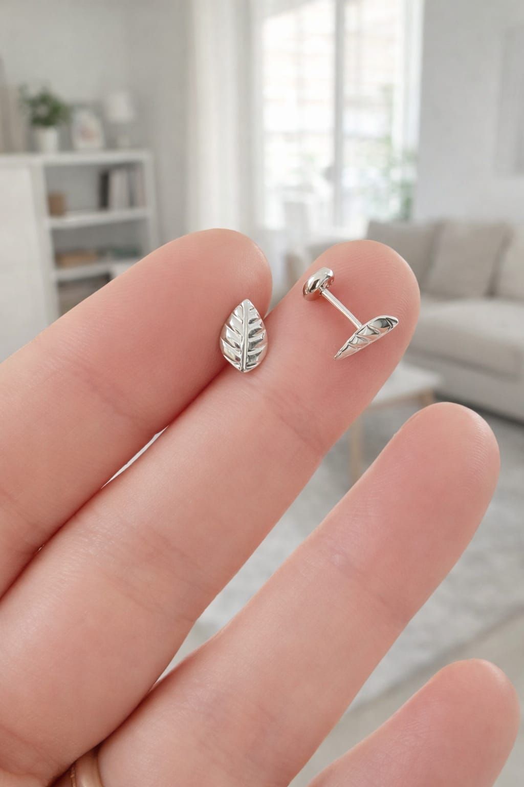 Pendiente pequeño de plata con forma de corazón, sostenido entre los dedos, con un fondo interior borroso.