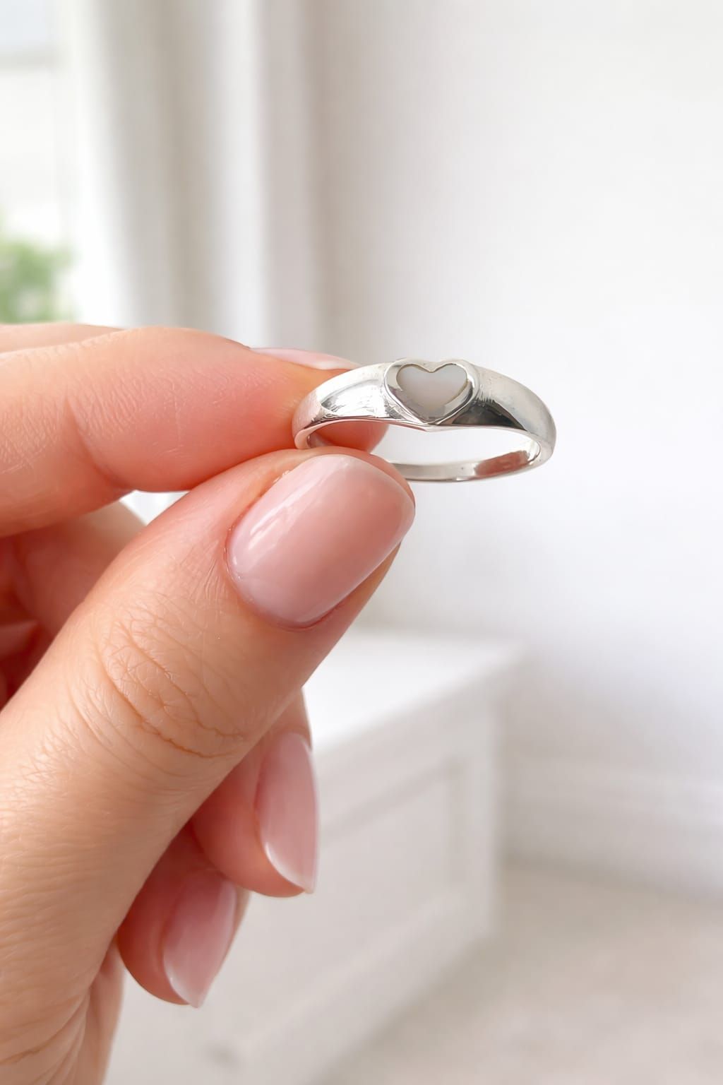 Una mano sostiene un anillo de plata brillante frente a una habitación blanca ligeramente borrosa.