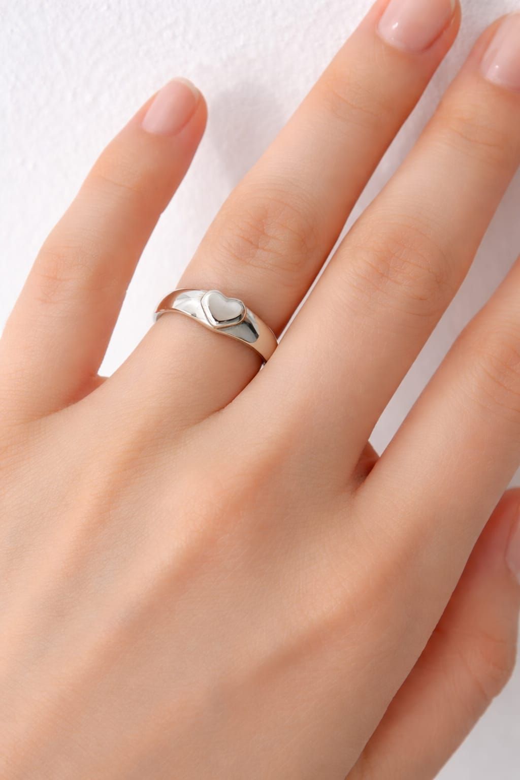 Una mano sostiene un anillo de plata brillante frente a una habitación blanca ligeramente borrosa.