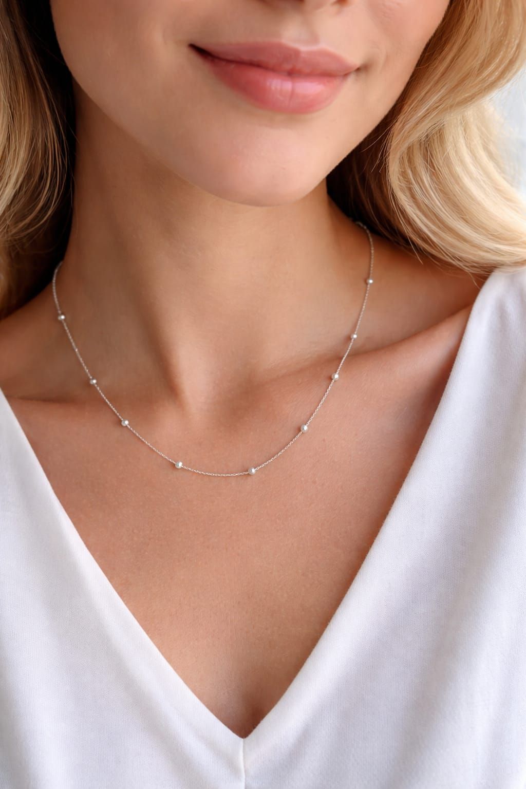 Primer plano de una mujer con un delicado collar de plata y una blusa blanca con escote en V.