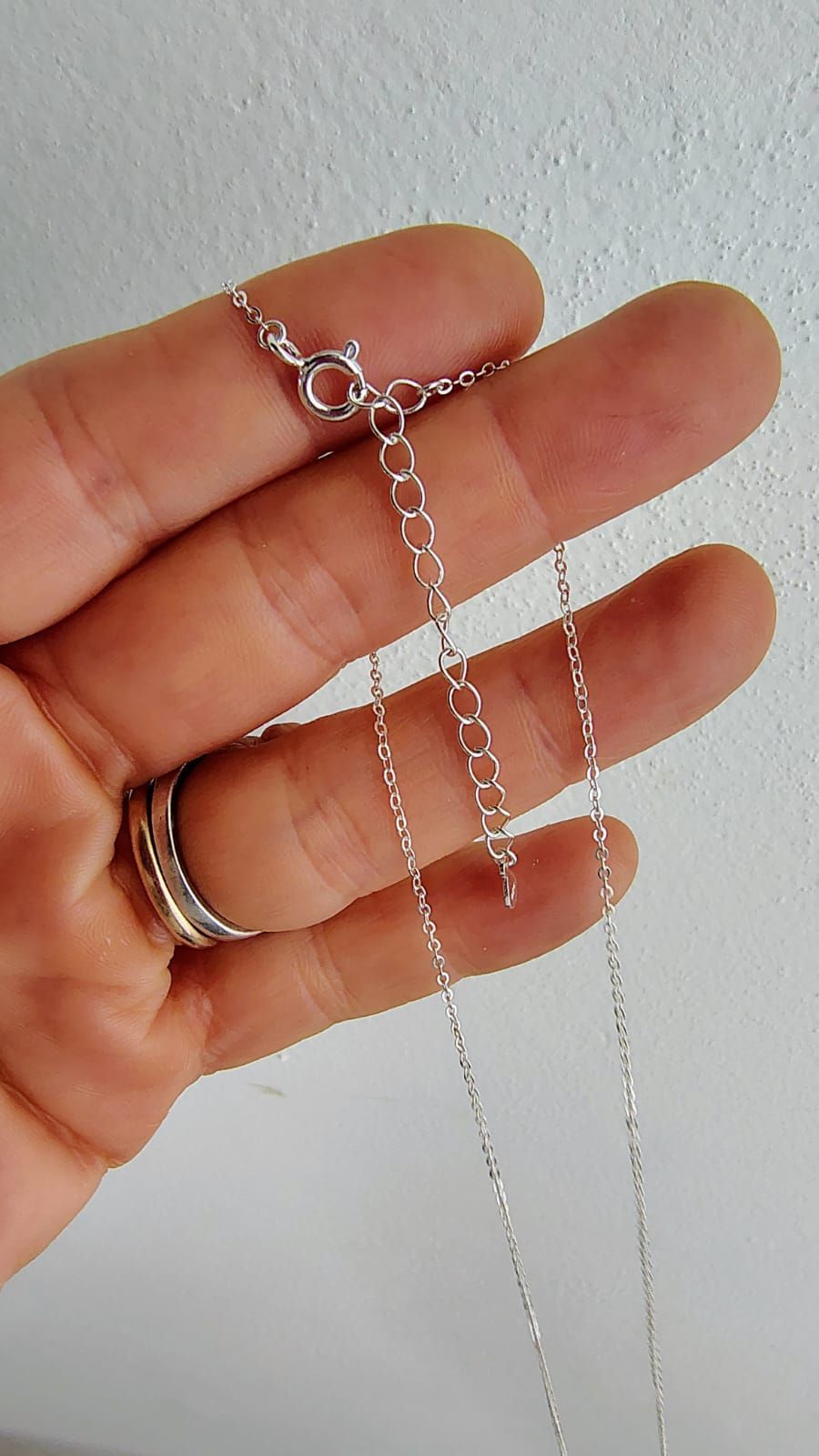 Delicado collar de plata en forma de V colgado de una mano sobre un fondo blanco.