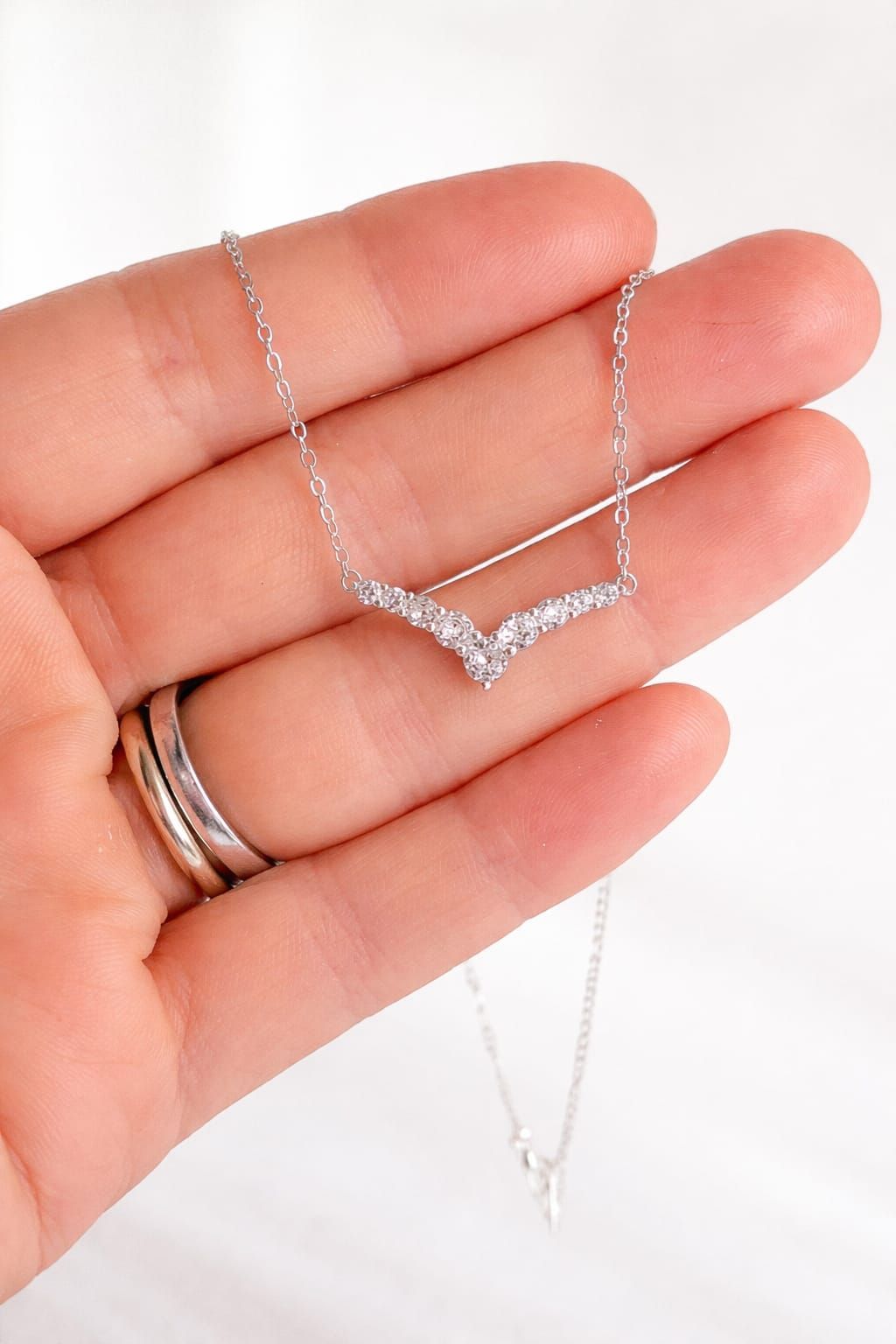 Delicado collar de plata en forma de V colgado de una mano sobre un fondo blanco.