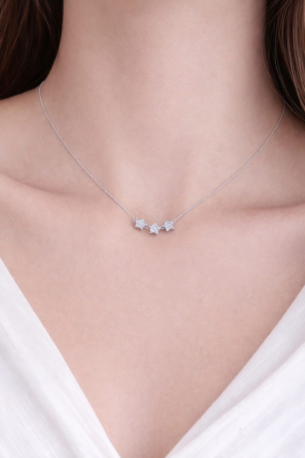 Collar de plata con un pequeño colgante sobre una blusa blanca con escote en V.