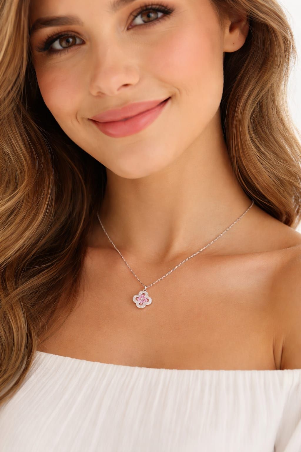 Mujer sonriente con un top blanco sin hombros y un delicado collar con colgante.