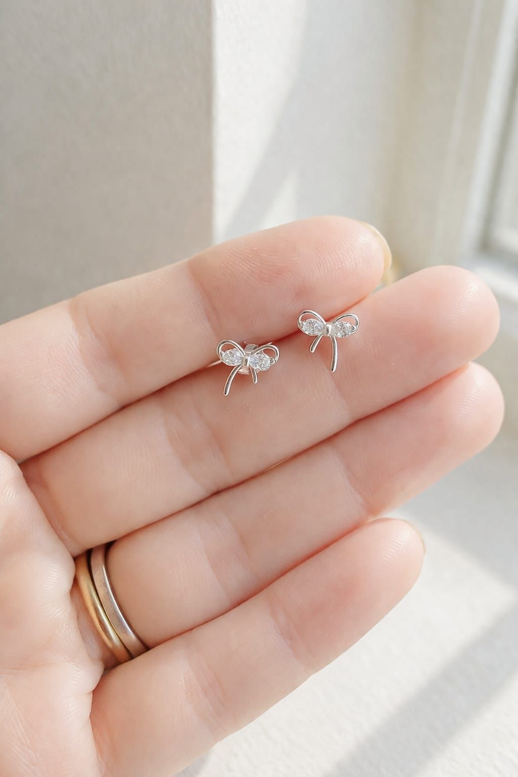 Mano sosteniendo dos pequeños pendientes de mariposa plateados con piedras transparentes.