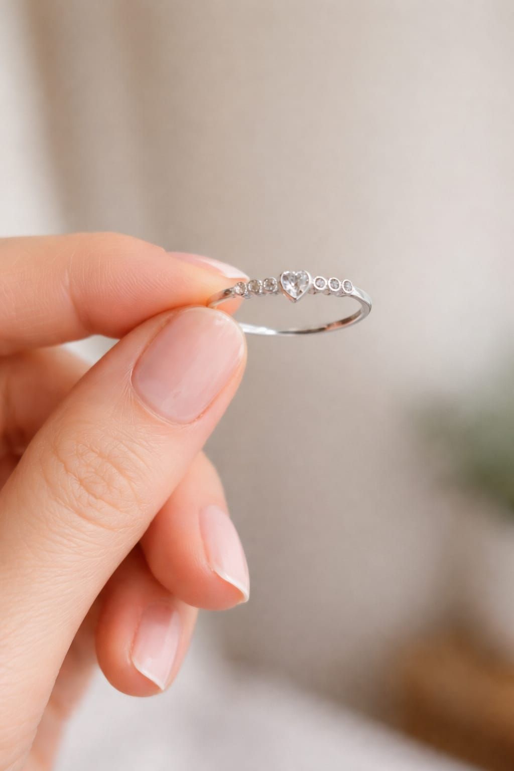 Primer plano de una mano que luce un delicado anillo de plata con pequeñas piedras sobre un fondo rosa pálido.