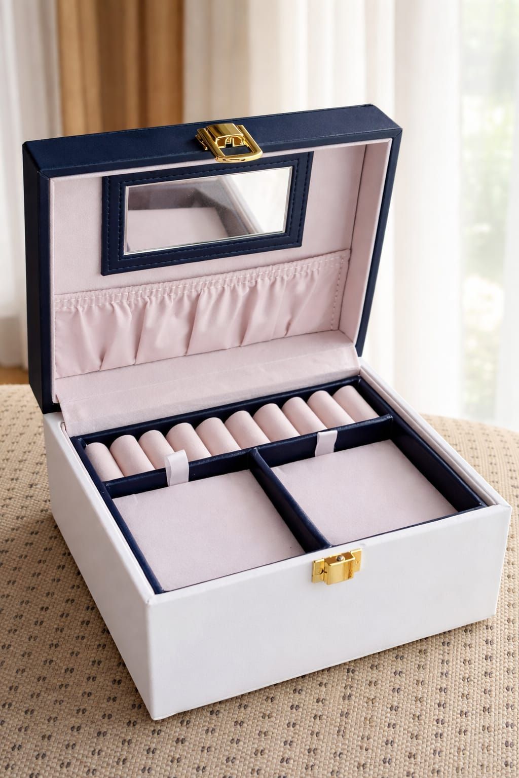 Pequeña caja decorativa en blanco y negro con cierre dorado sobre una mesa de mimbre cerca de una ventana.