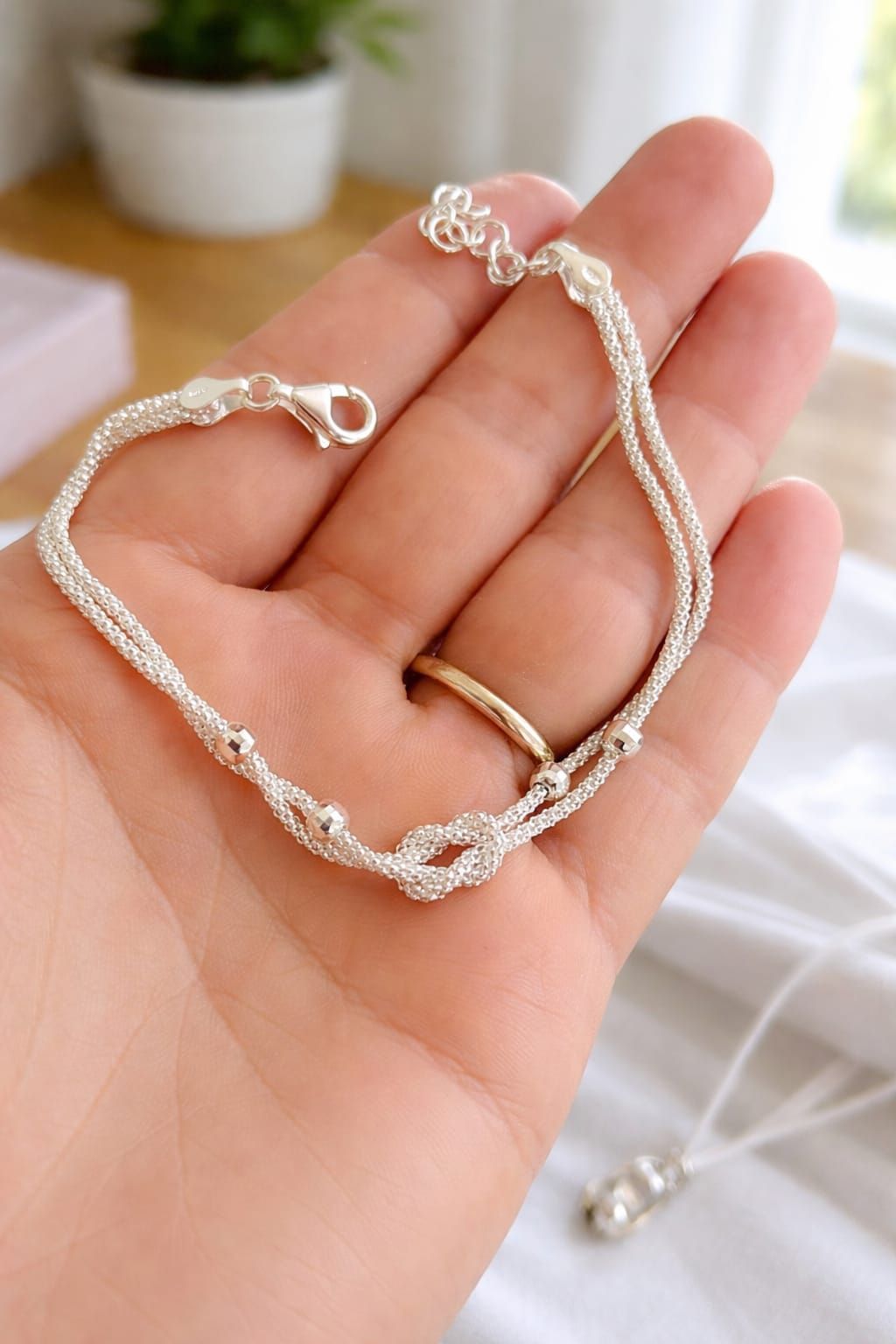 Pulsera de plata con cierre en forma de corazón que descansa sobre una palma abierta.