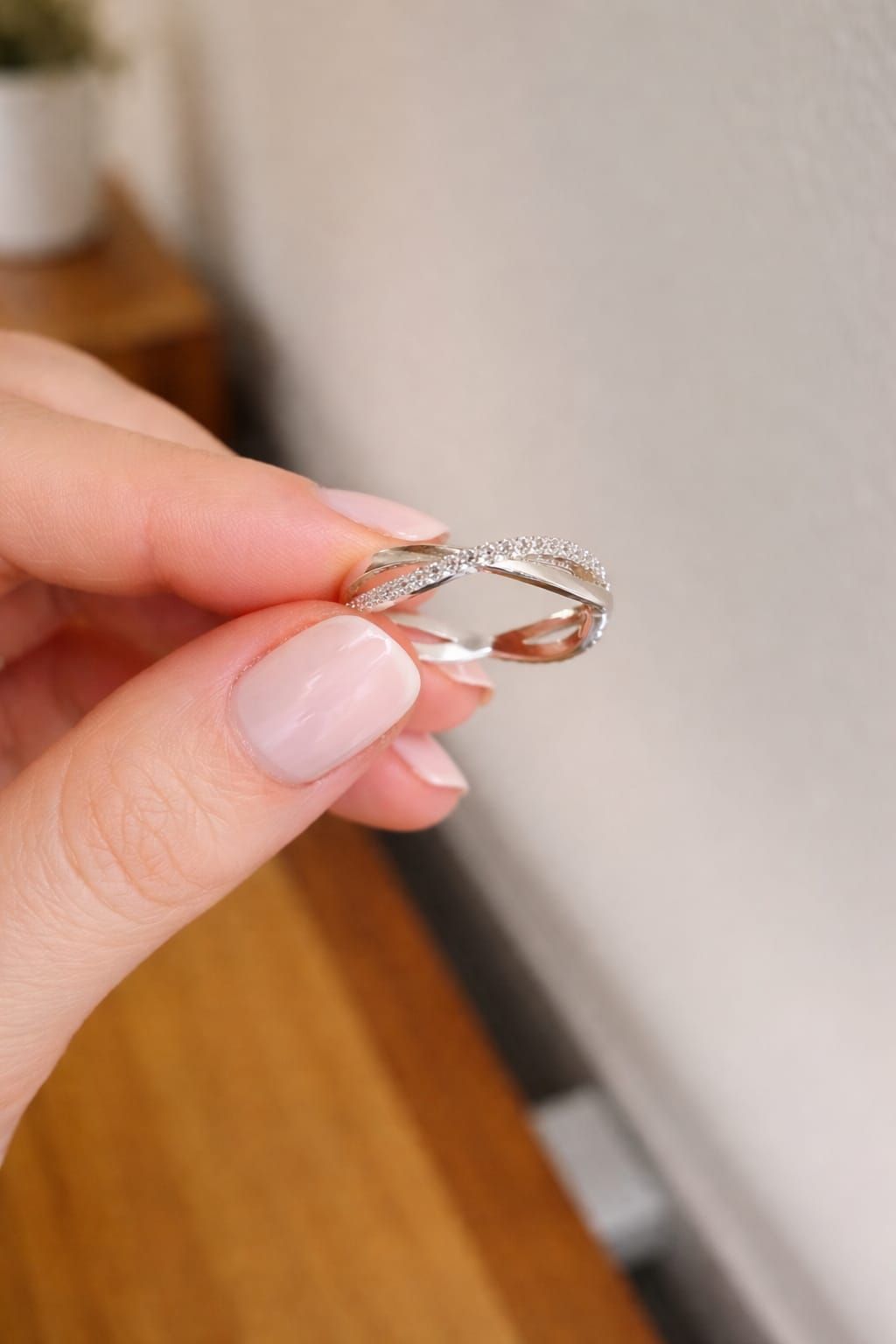 Mano sosteniendo un anillo de plata con un diseño retorcido y pequeñas piedras sobre un fondo interior borroso.