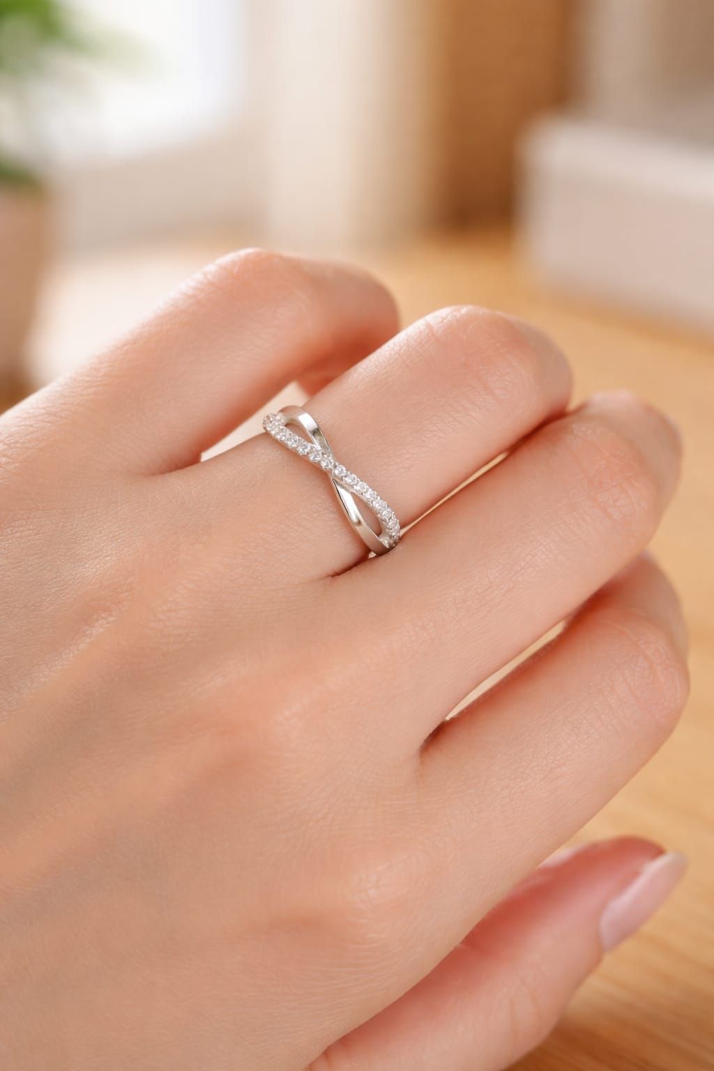 Mano sosteniendo un anillo de plata con un diseño retorcido y pequeñas piedras sobre un fondo interior borroso.