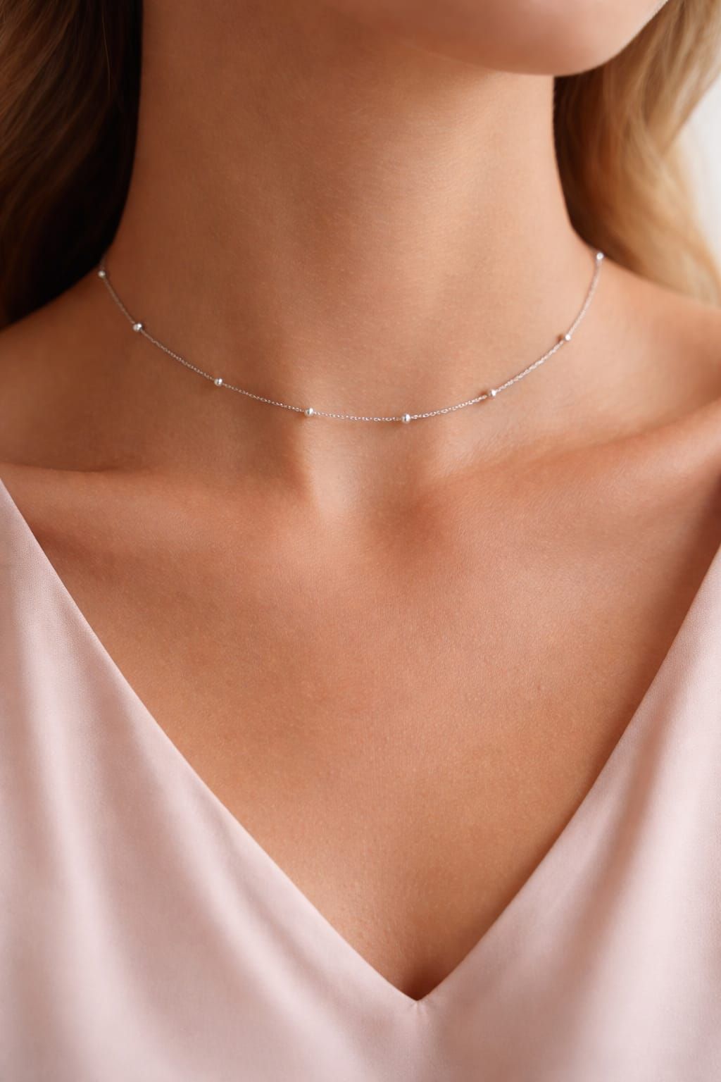 Collar de plata delicado en una persona que lleva una blusa rosa pálido con escote en V.