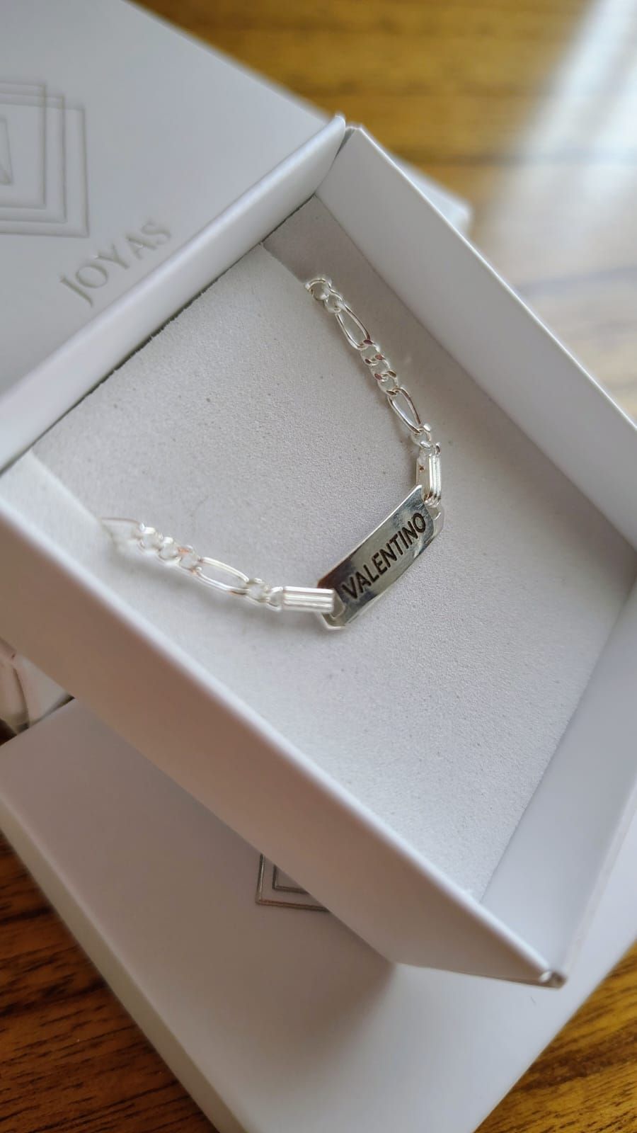 Pulsera de plata en un joyero blanco sobre una superficie de madera.