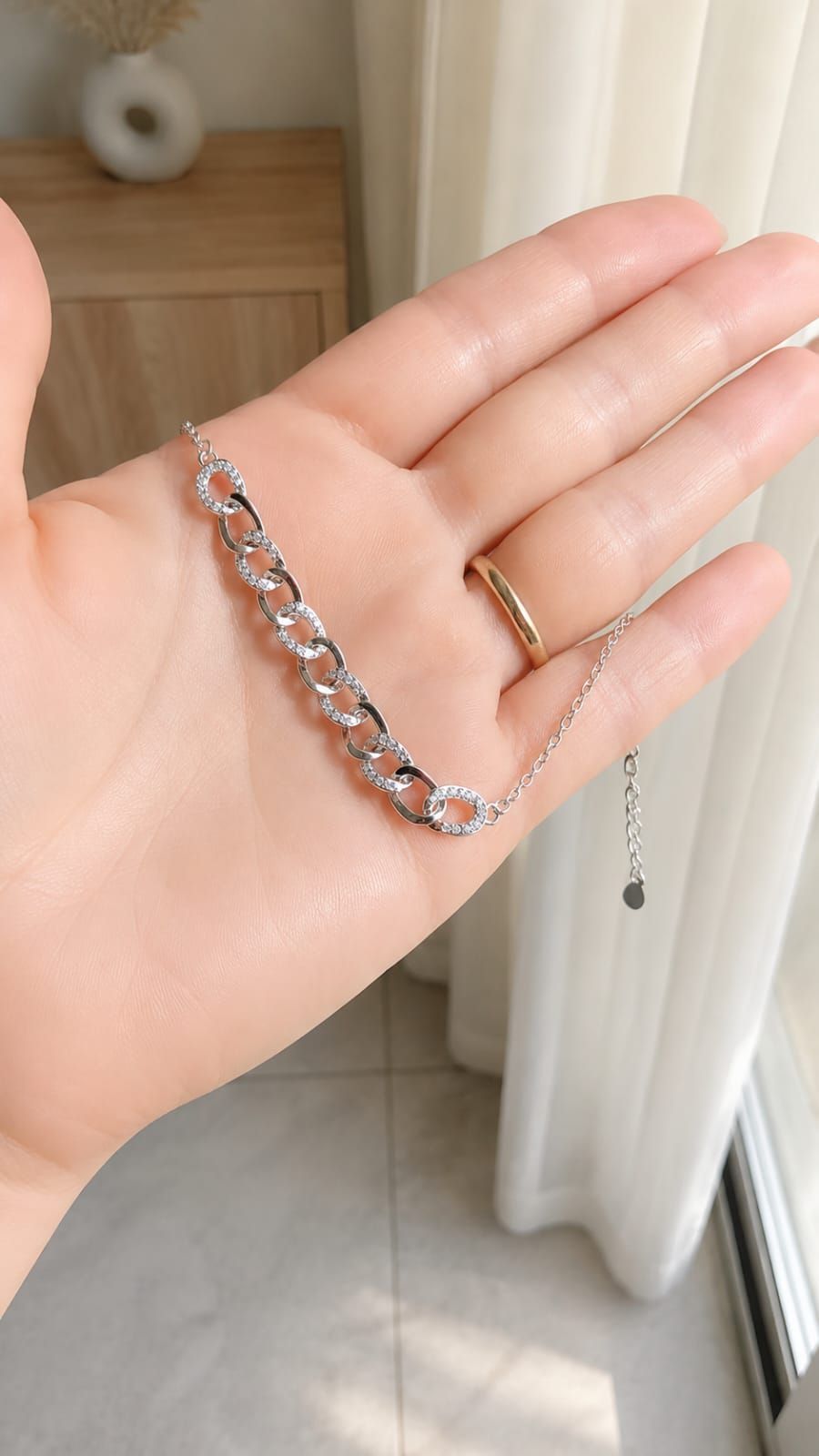 Muñeca con pulsera de plata con piedras transparentes sobre un fondo suave de interior.