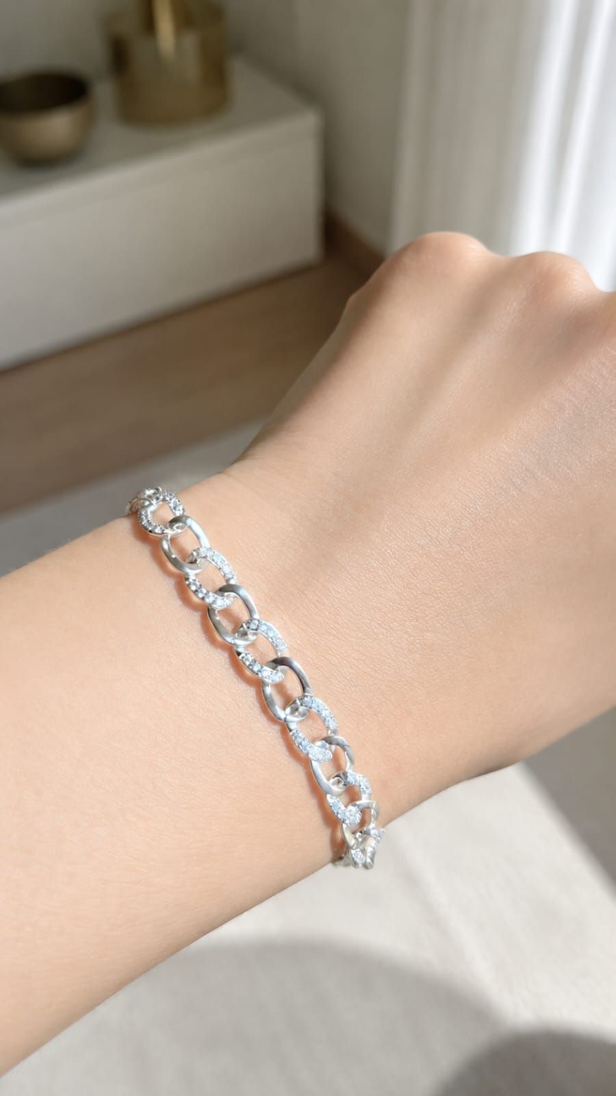 Muñeca con pulsera de plata con piedras transparentes sobre un fondo suave de interior.