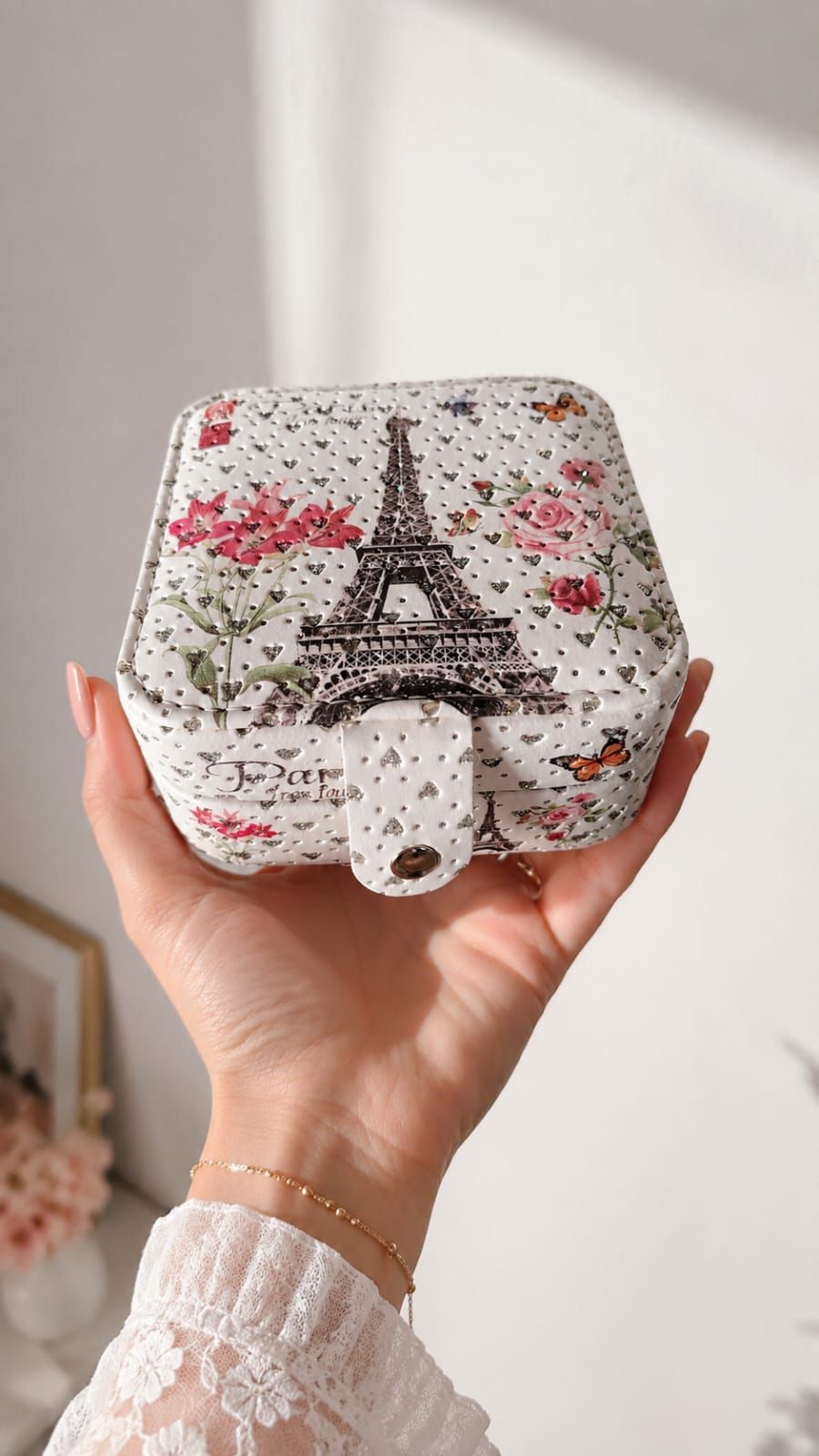 Mano sosteniendo un bolso blanco con estampado floral, diseño de la Torre Eiffel y detalles en rosa.