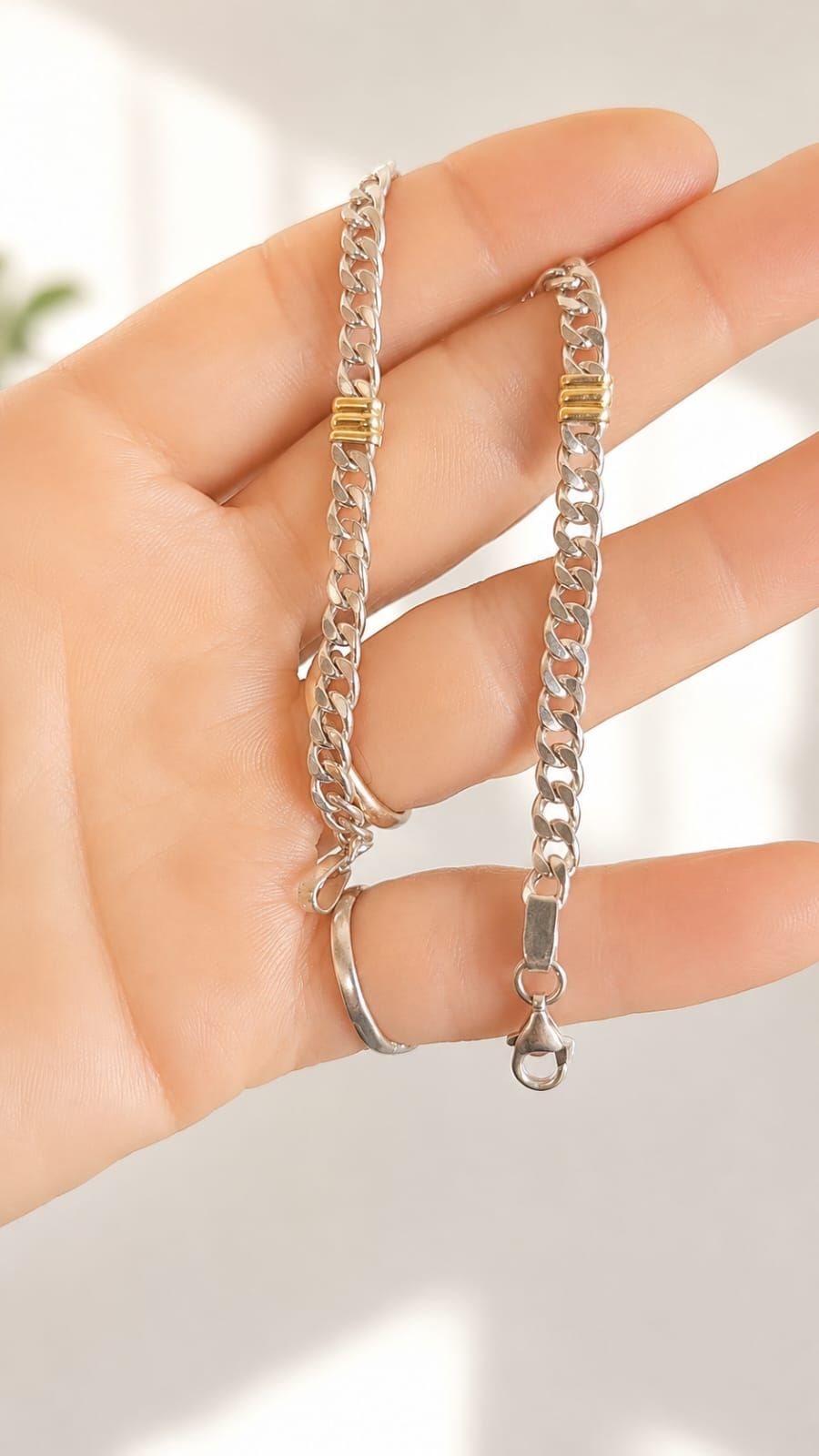 Una mano sosteniendo una delicada pulsera de cadena de oro con un pequeño cierre sobre un fondo claro.