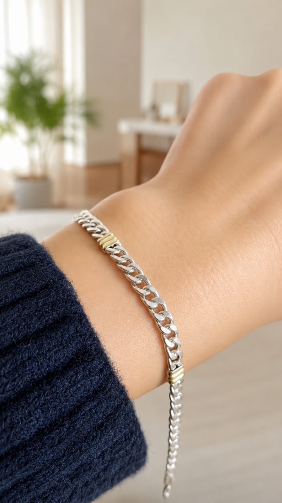 Una mano sosteniendo una delicada pulsera de cadena de oro con un pequeño cierre sobre un fondo claro.