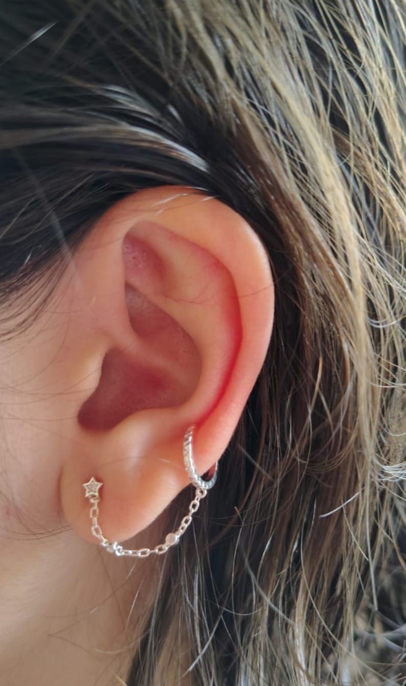 Primer plano de una oreja con un pendiente de cadena plateada y cabello oscuro.