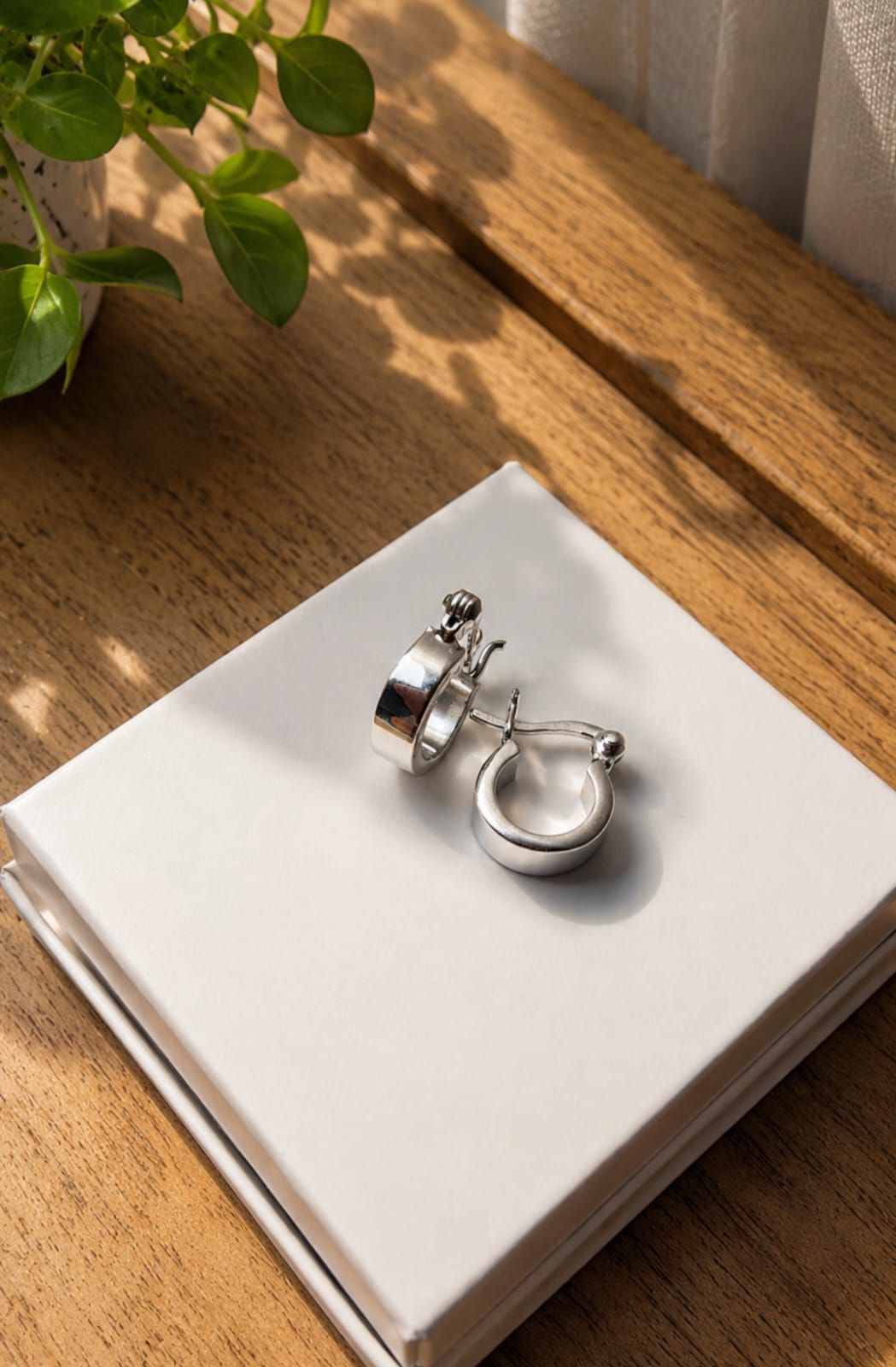 Anillos de plata sobre un libro blanco en una mesa de madera junto a una ventana iluminada por el sol.