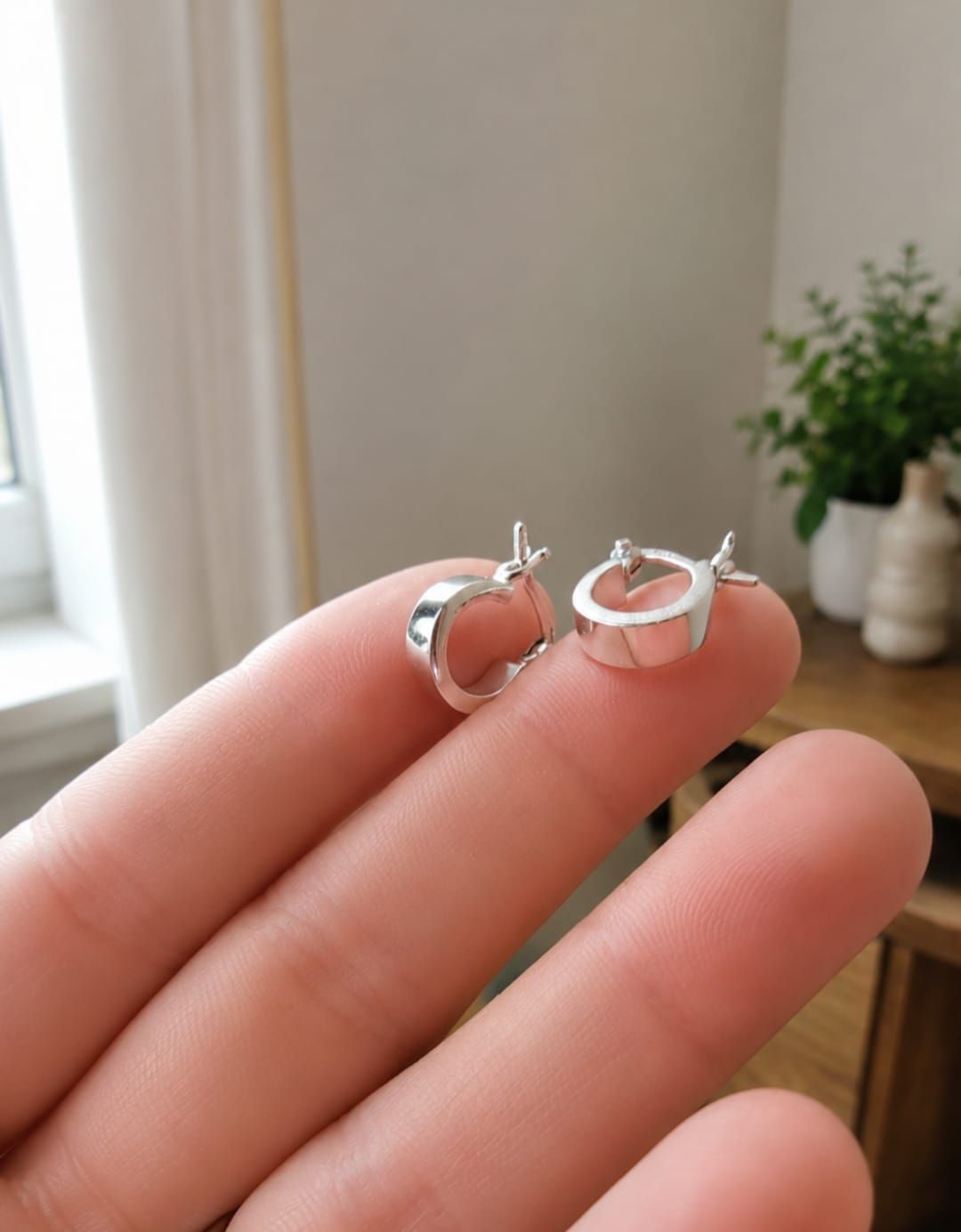 Anillos de plata sobre un libro blanco en una mesa de madera junto a una ventana iluminada por el sol.
