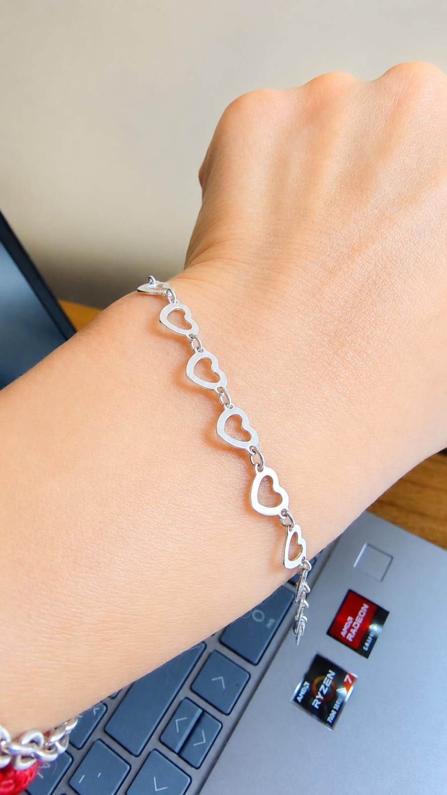 Mano sosteniendo un delicado collar de cadena de plata con eslabones en forma de corazón en el interior.