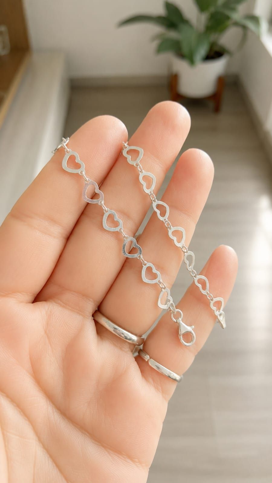 Mano sosteniendo un delicado collar de cadena de plata con eslabones en forma de corazón en el interior.