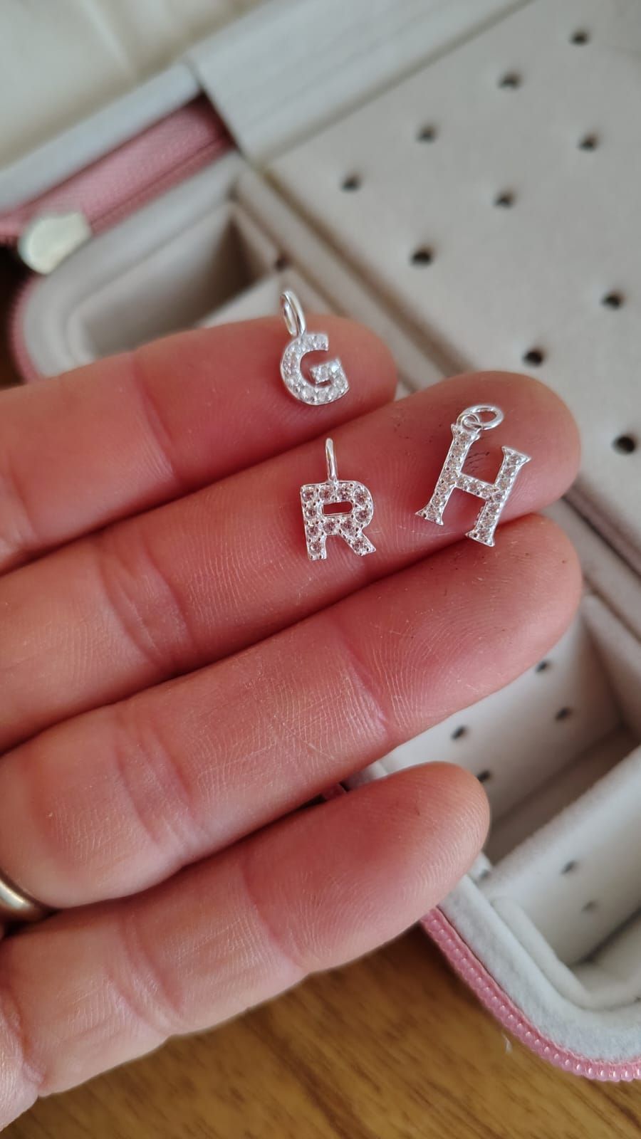 Una mano sostiene un collar de plata con un colgante brillante con la letra M en el interior de una vivienda.
