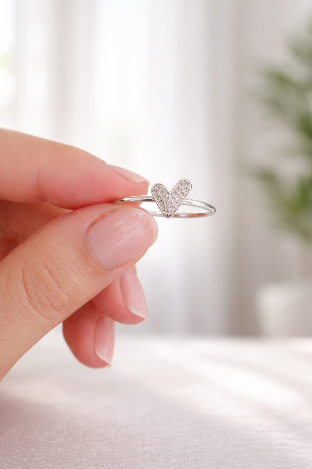 Mano con un anillo de mariposa de plata sobre un fondo rosa suave