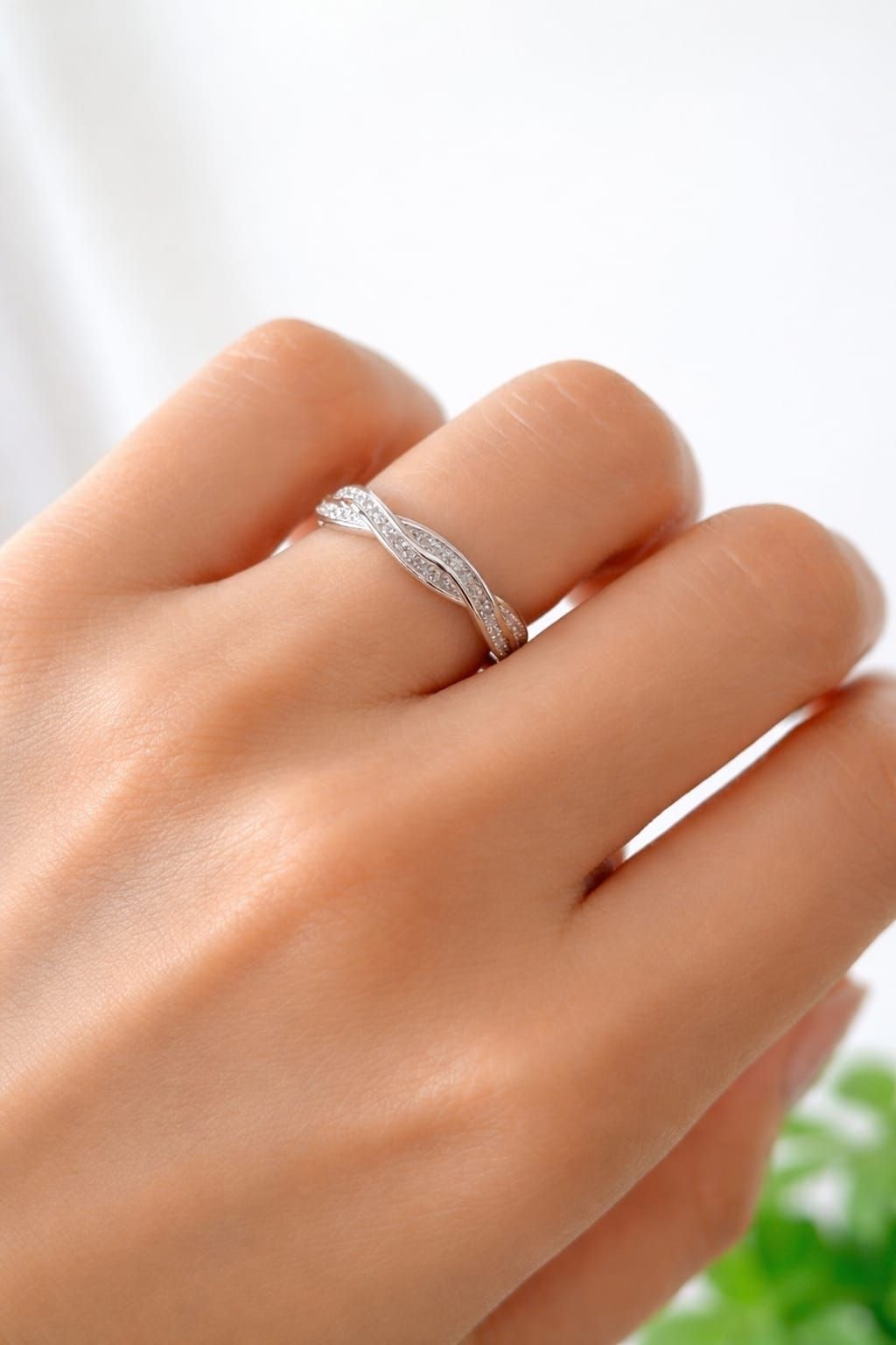 Mano con un anillo de plata con pequeñas piedras brillantes sobre un fondo blanco suave.