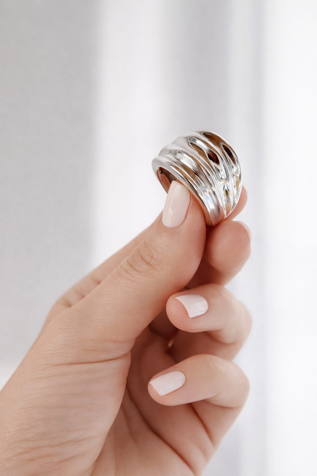 Mano con uñas blancas luciendo un anillo plateado apilado sobre un fondo blanco.