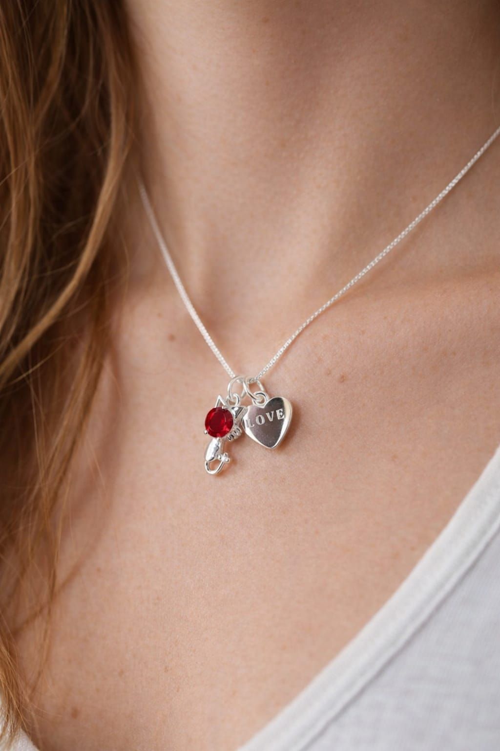 Collar de plata con colgantes de corazón y piedras preciosas rojas en el cuello y el pecho de una mujer.