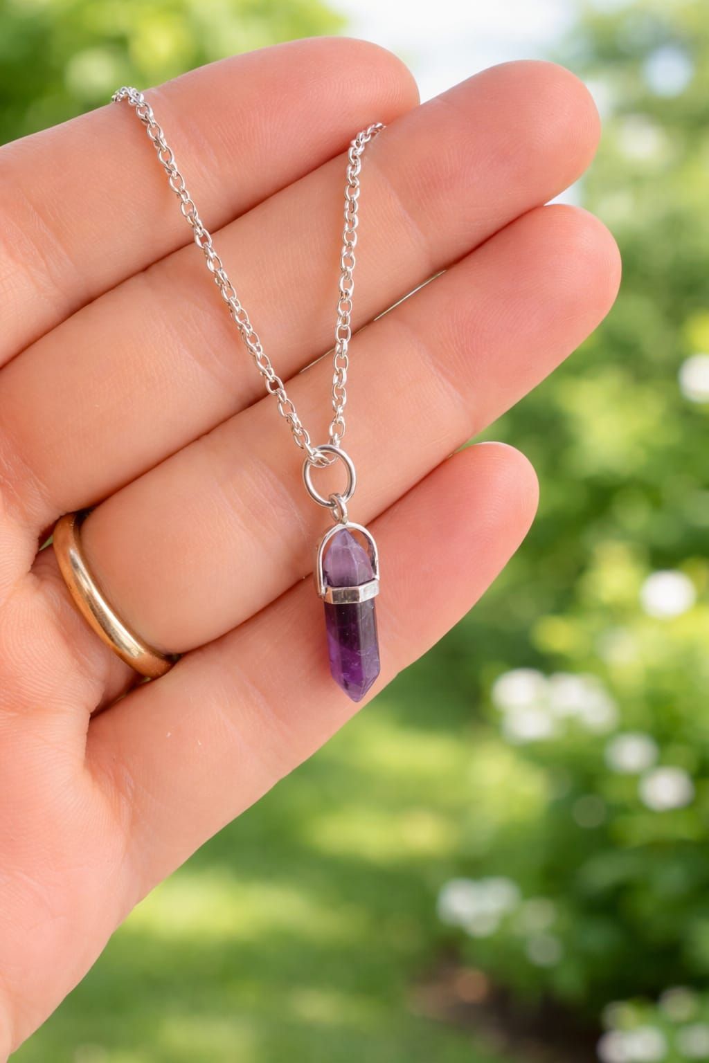 Tres collares colgantes de cristal con las etiquetas cuarzo rosa, amatista y turquesa sobre un fondo rosa suave.