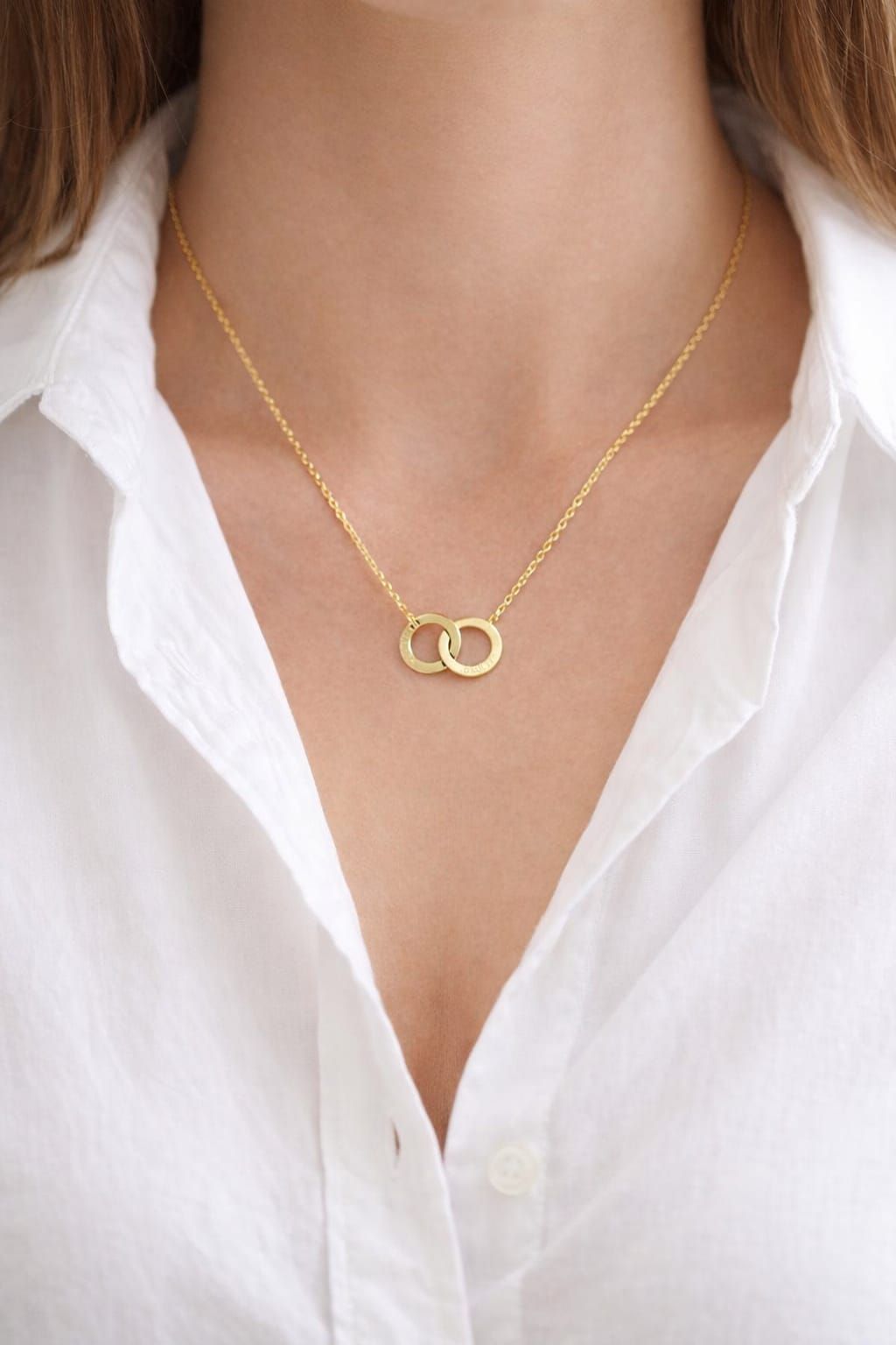 Collar de oro con anillos entrelazados sobre el cuello de una camisa blanca.