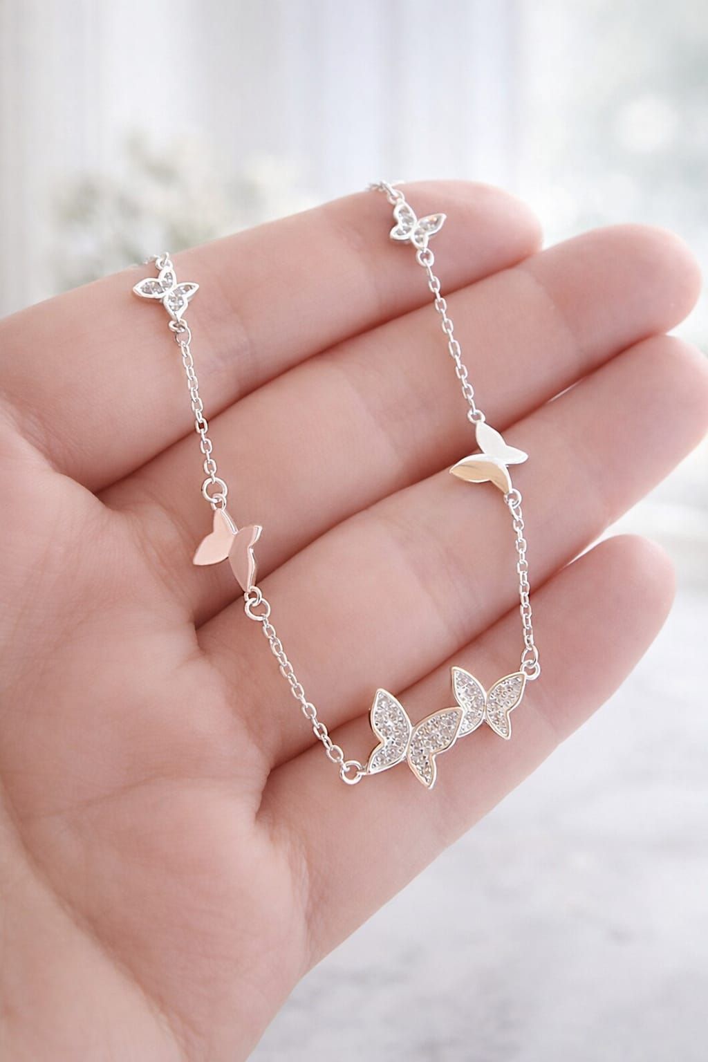 Pulsera plateada con dije de mariposa en la muñeca, adornada con estrellas y corazones colgantes.