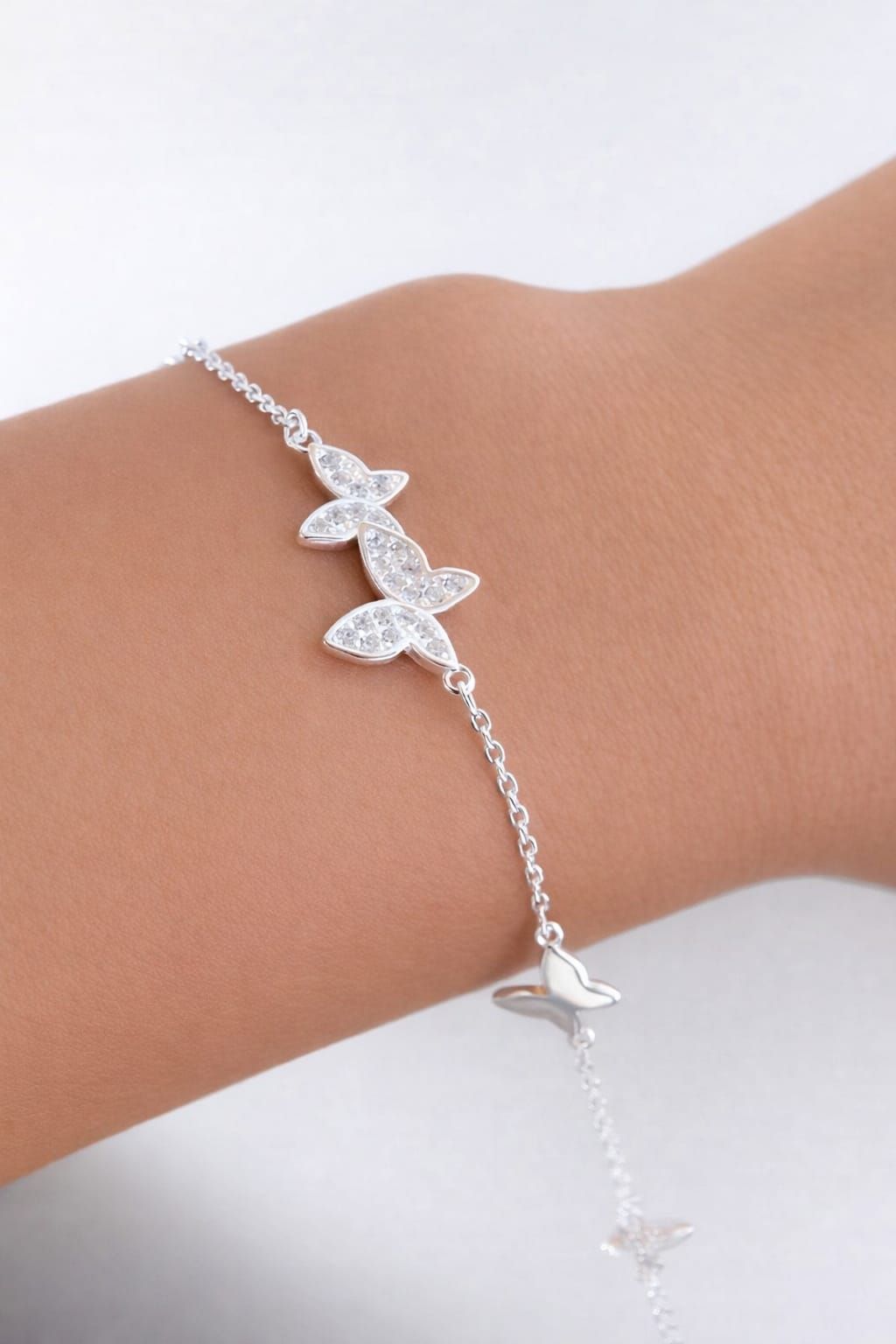 Pulsera plateada con dije de mariposa en la muñeca, adornada con estrellas y corazones colgantes.