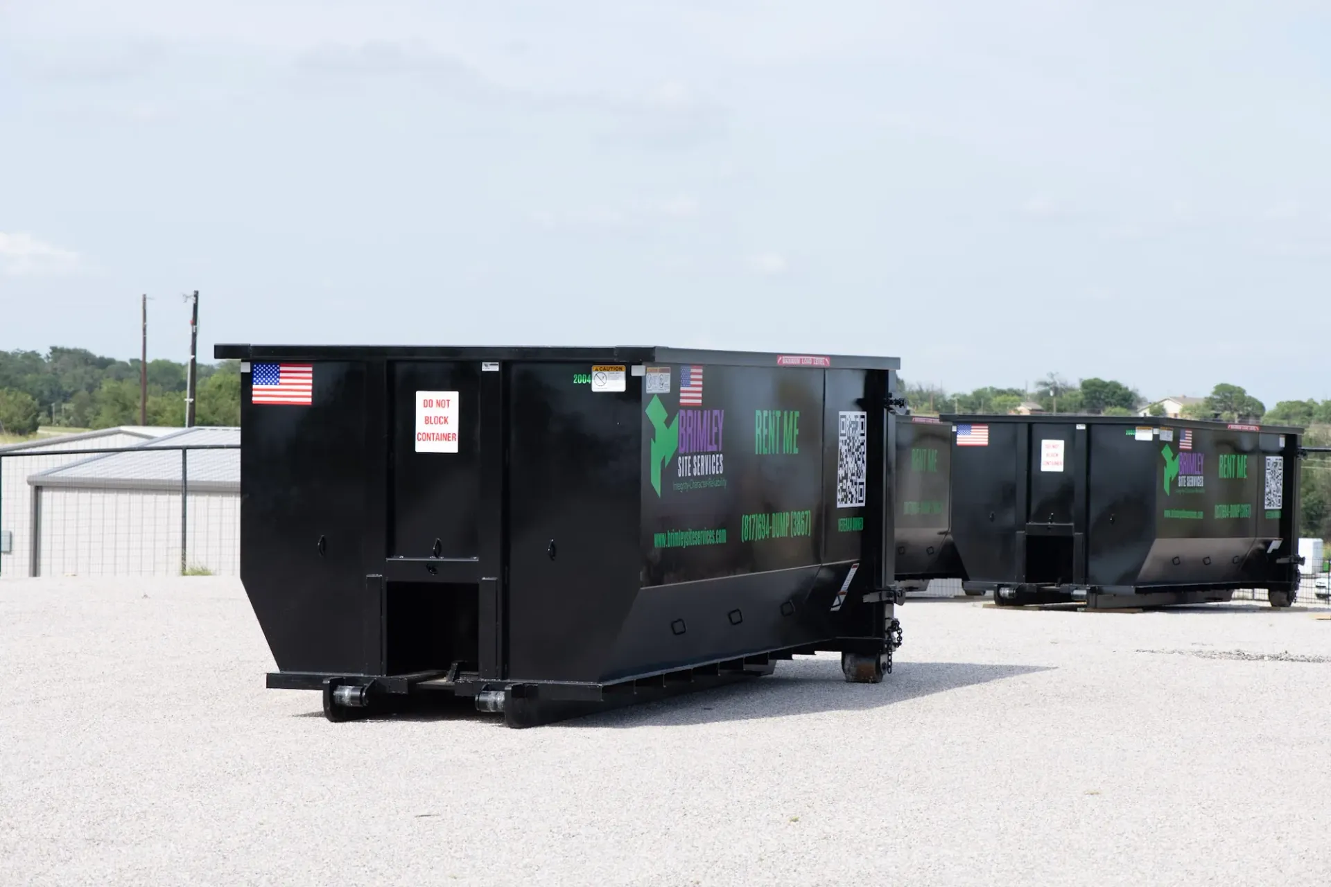 A row of dumpsters are parked in a gravel lot.