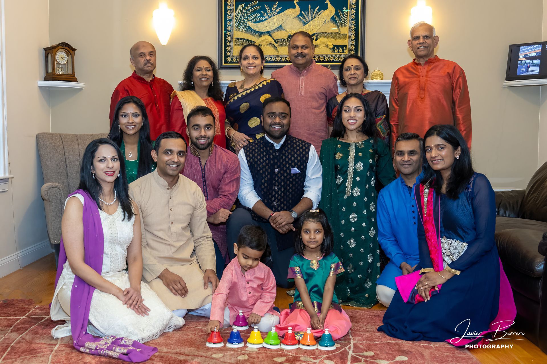 Group of people posing indoors around a festive rangoli, smiling in traditional attire.