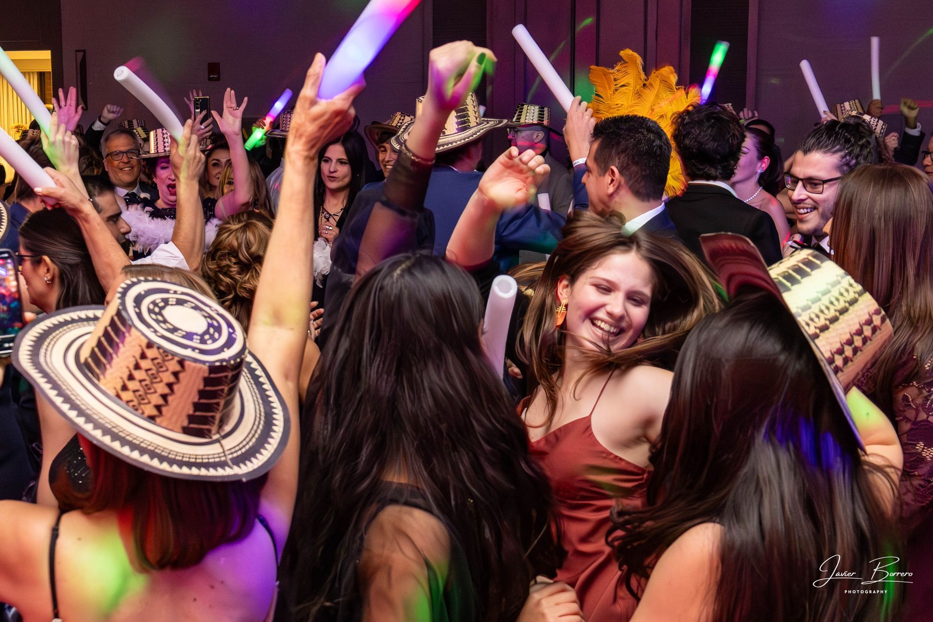 Crowded dance floor with people cheering, raised glow sticks, and colorful lights at a festive party