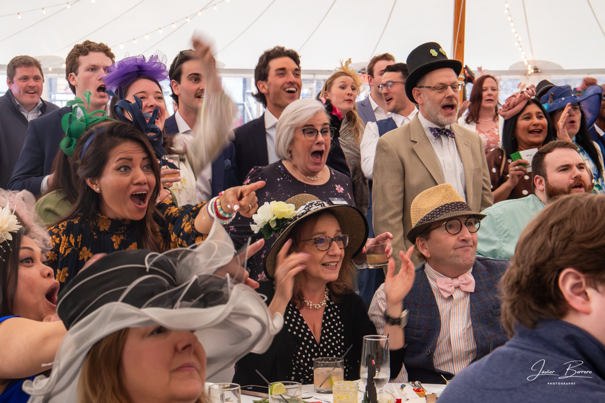 Crowd of people in hats cheering and smiling at an indoor event with a festive, lively atmosphere