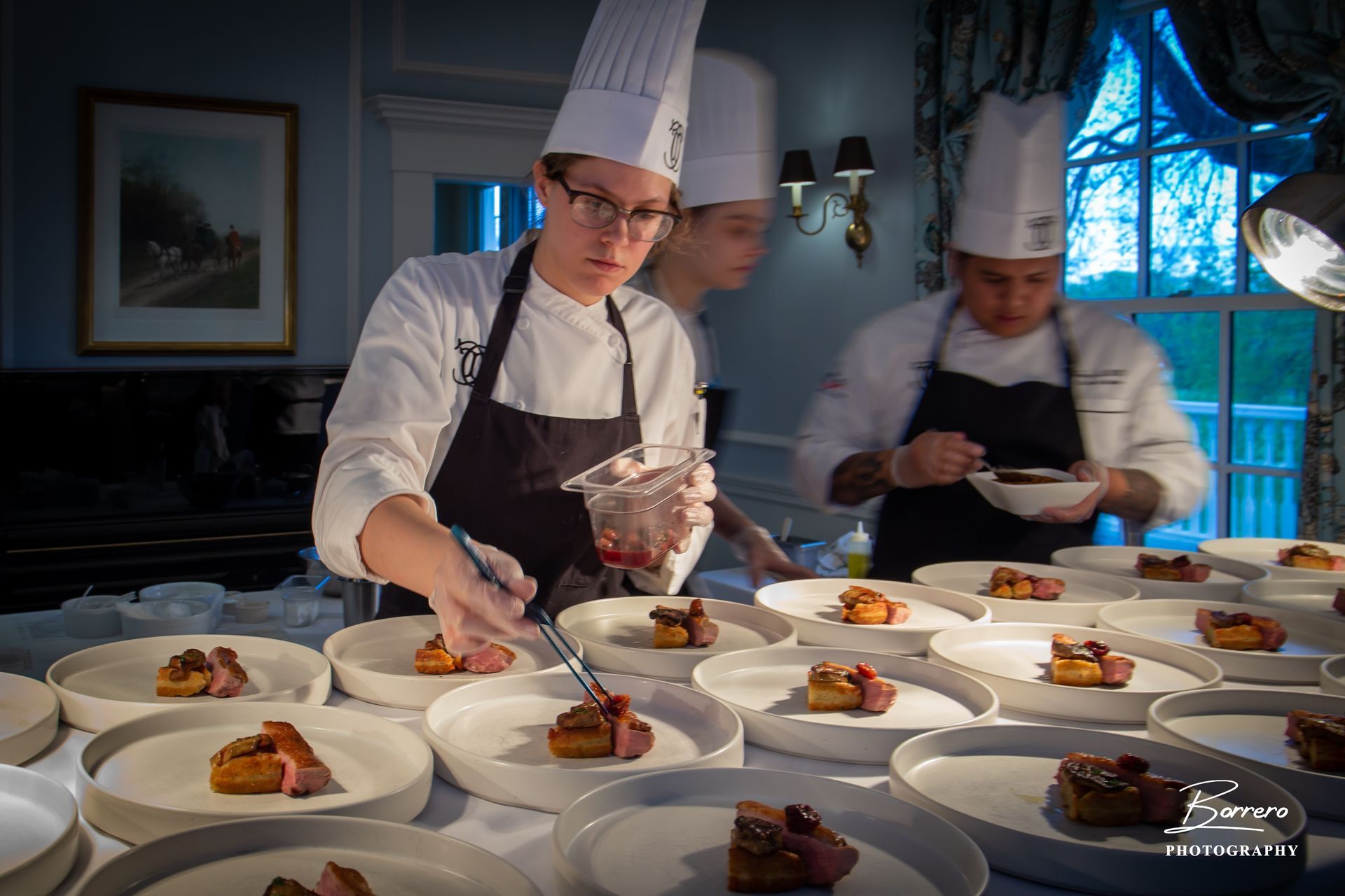 Three chefs in uniforms and hats carefully plate gourmet food in a professional kitchen.