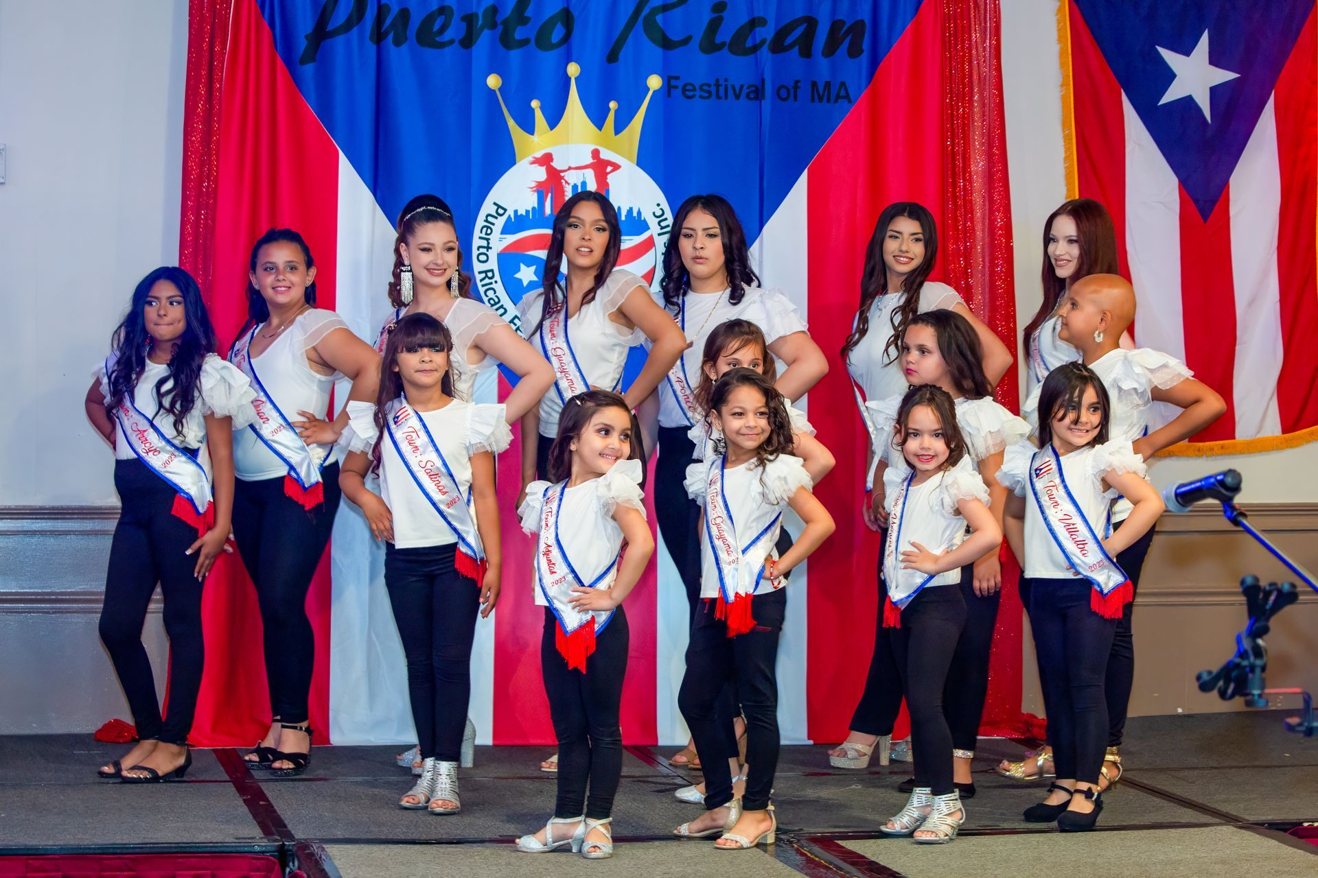 Large group in colorful costumes posing outdoors under a pavilion, holding a Puerto Rican flag.