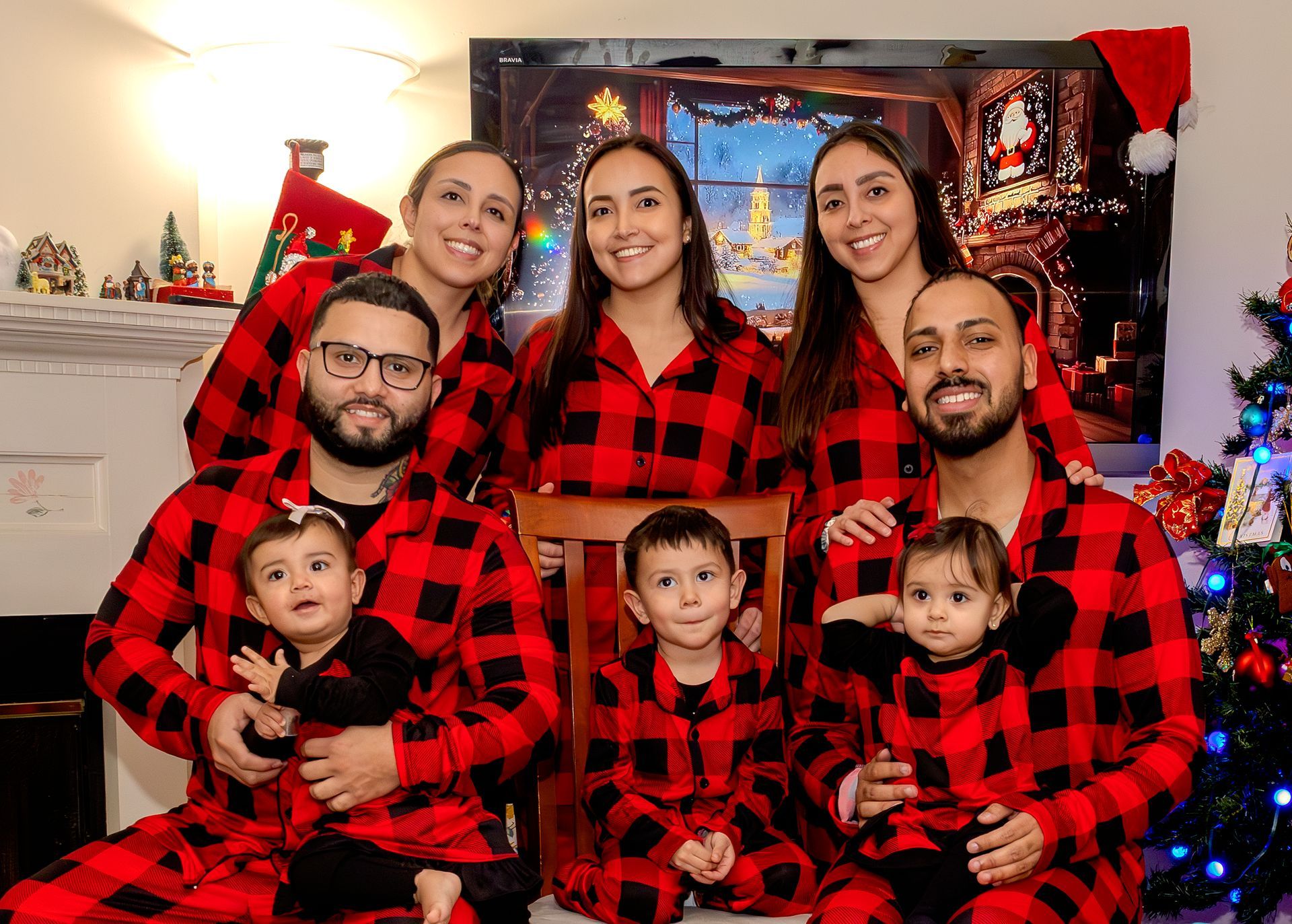 Family in red plaid pajamas posing together in a decorated living room with Christmas lights and a tree