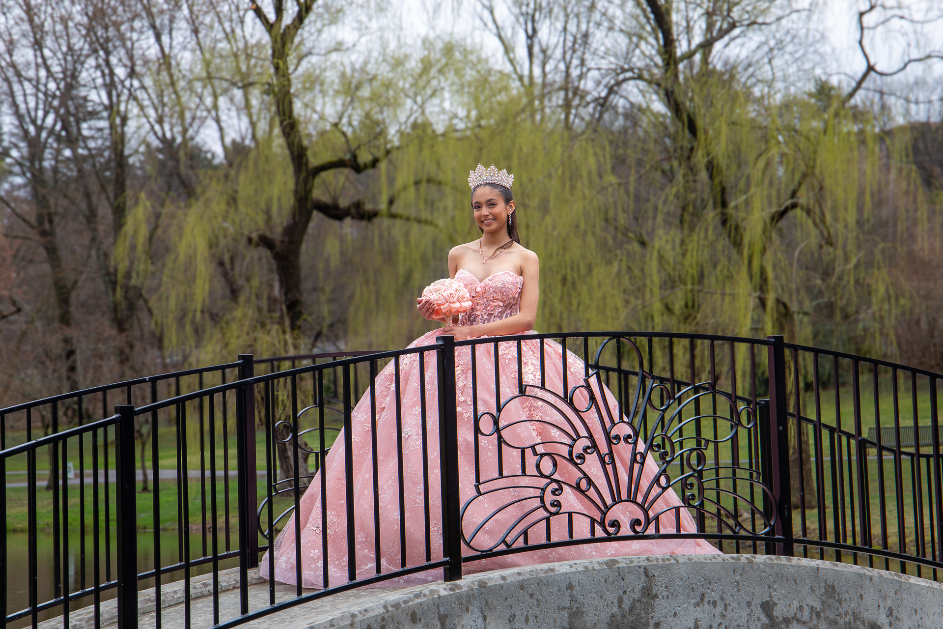 Woman in a pink ball gown standing on a bridge in a wooded park