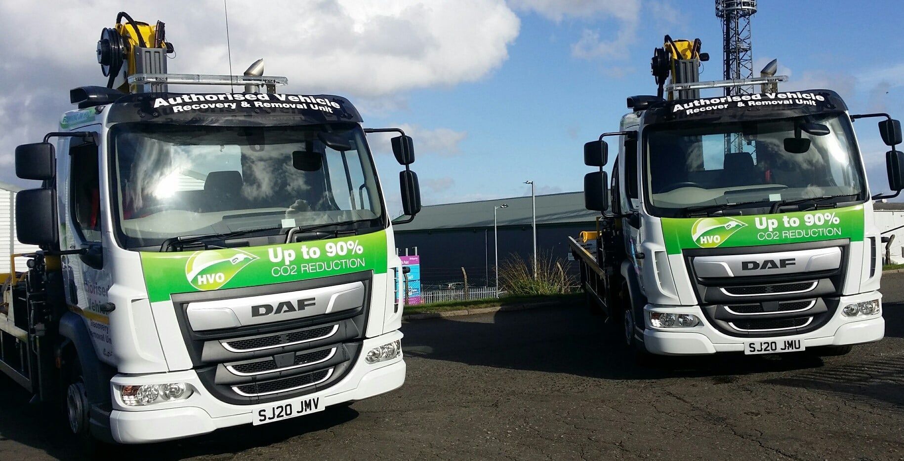 Two white DAF trucks with green accents parked outside, each with a crane on top.