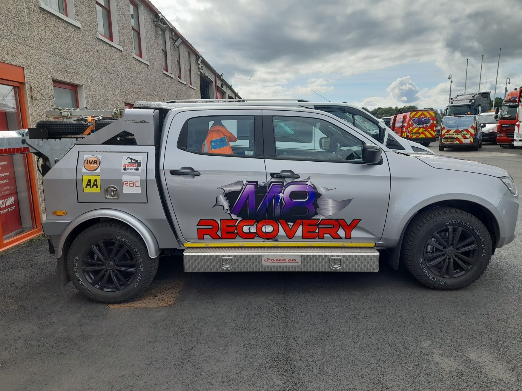 Silver recovery truck parked outside a building, with black wheels and 