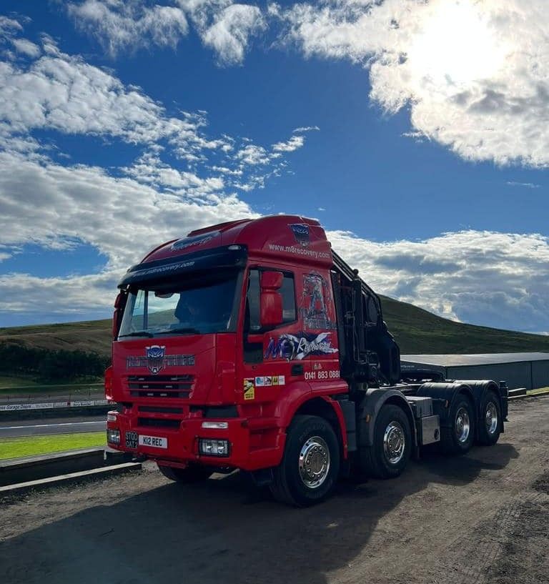 Red semi-truck with crane against a bright blue sky with clouds.