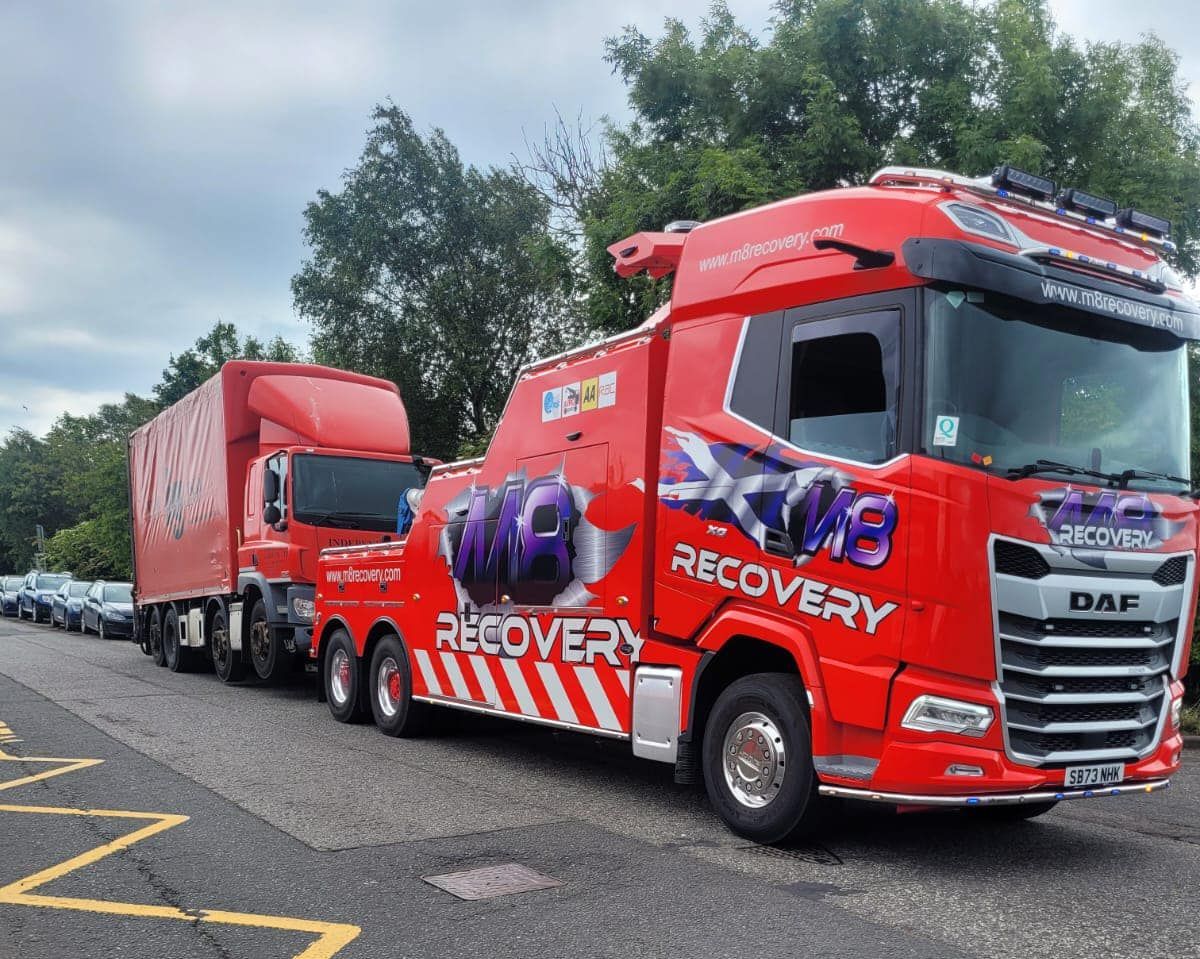 Red recovery truck with trailer, parked on a road. 